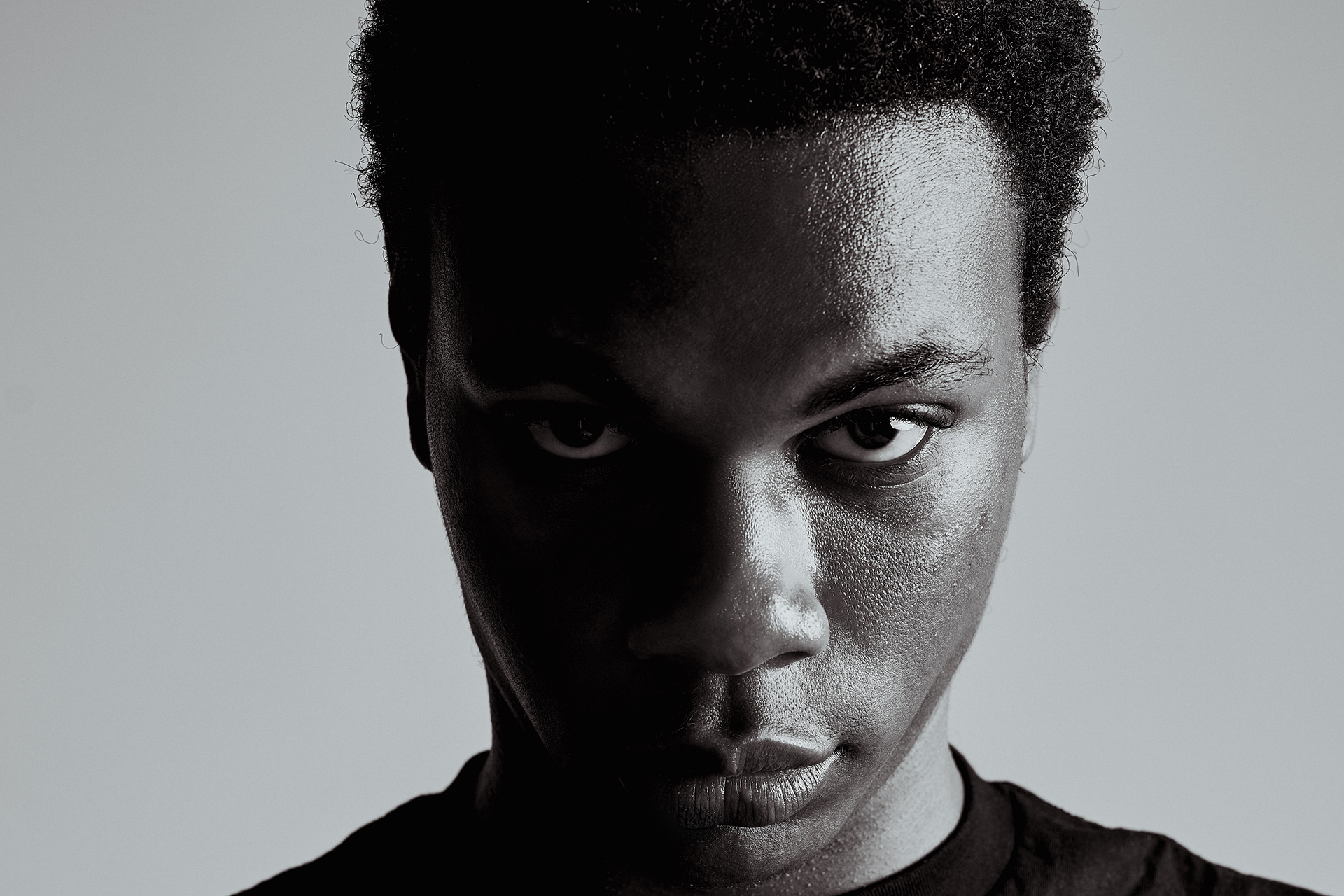 Black-and-white portrait with a serious, intense expression, dramatic studio lighting