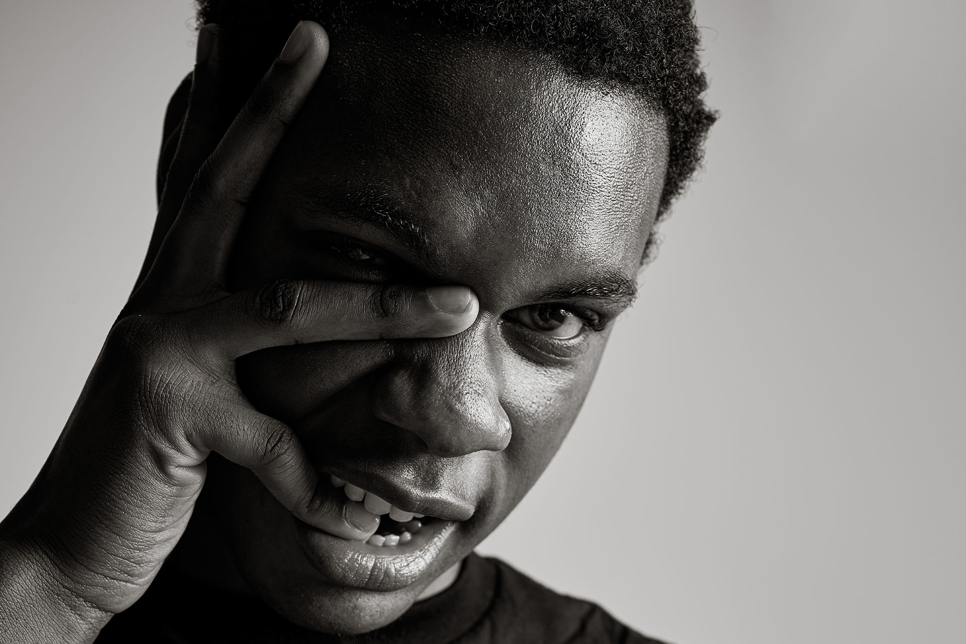 Black-and-white portrait with hand near the face and an intense expression, high-contrast lighting