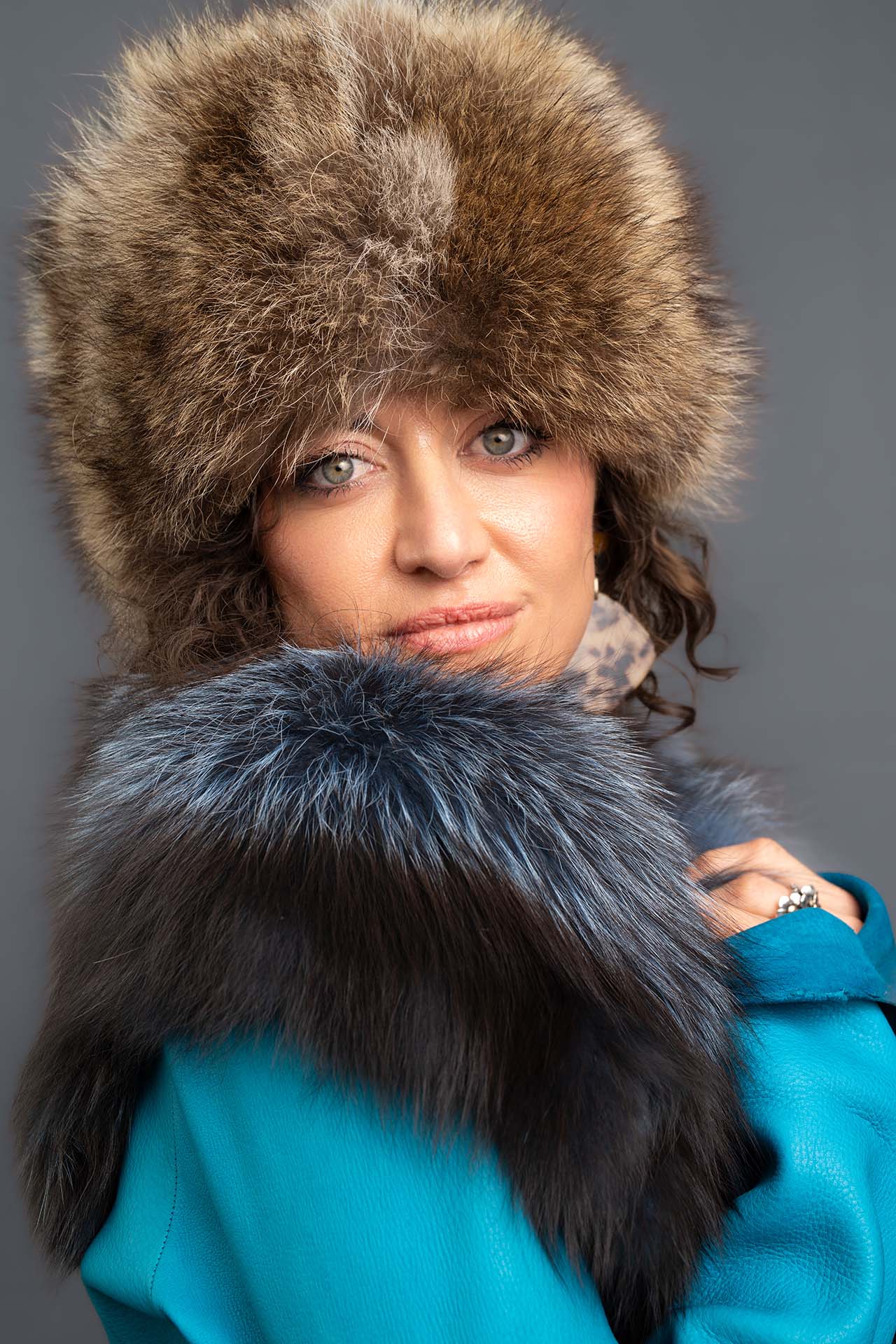 Model in a brown fur hat and teal fur collar, editorial studio portrait