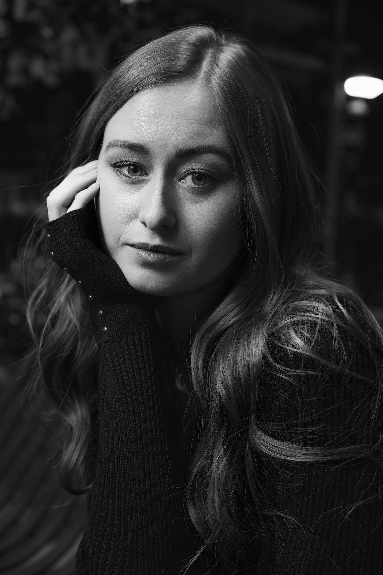 Black-and-white dramatic portrait with hand resting near the face, wavy hair, moody lighting