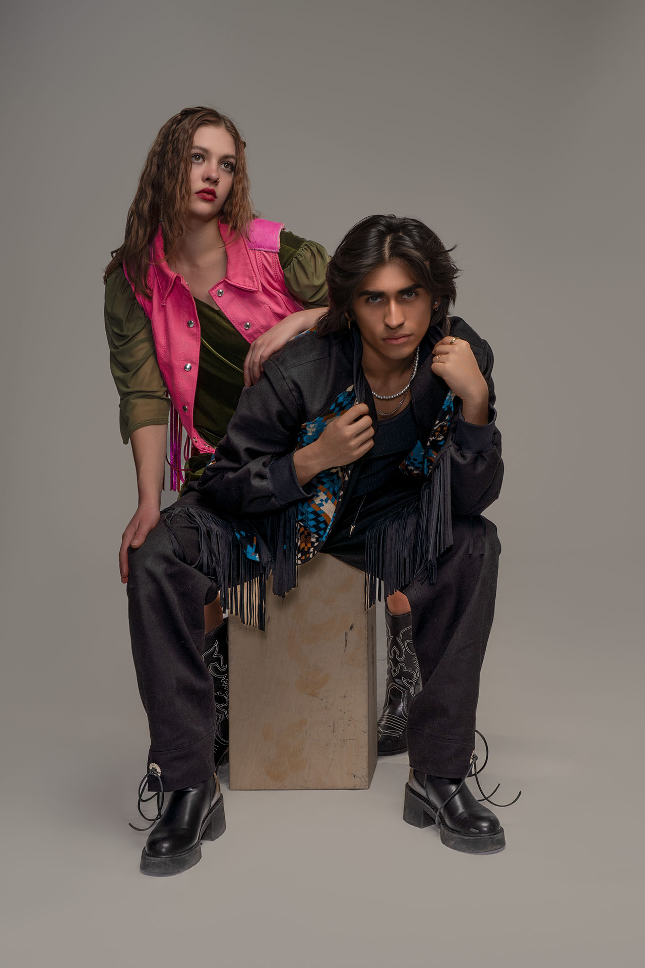 Two models in edgy western-inspired styling, pink and green jackets, seated editorial portrait