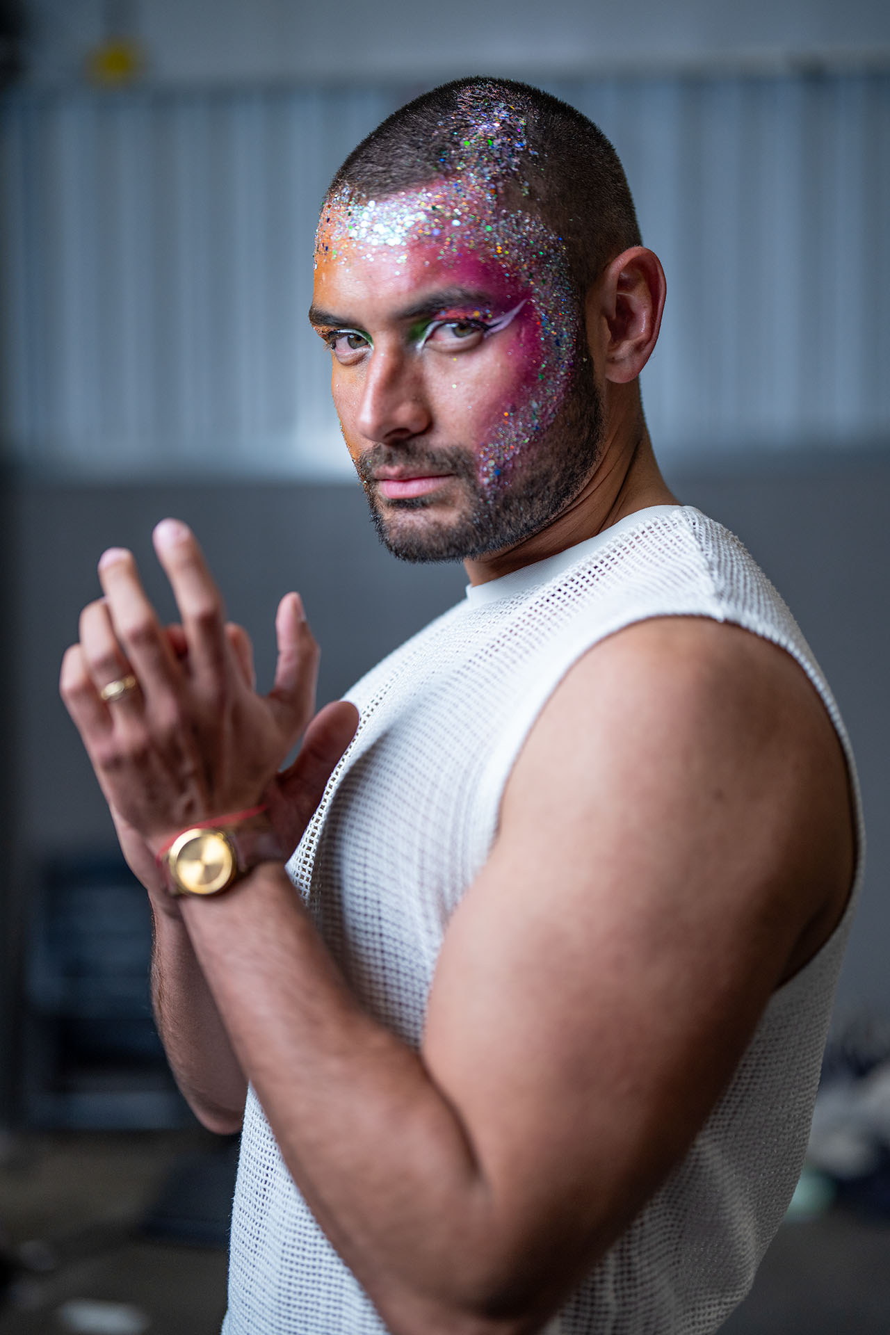 Portrait of a man with pink and silver glitter face paint, dramatic backstage lighting
