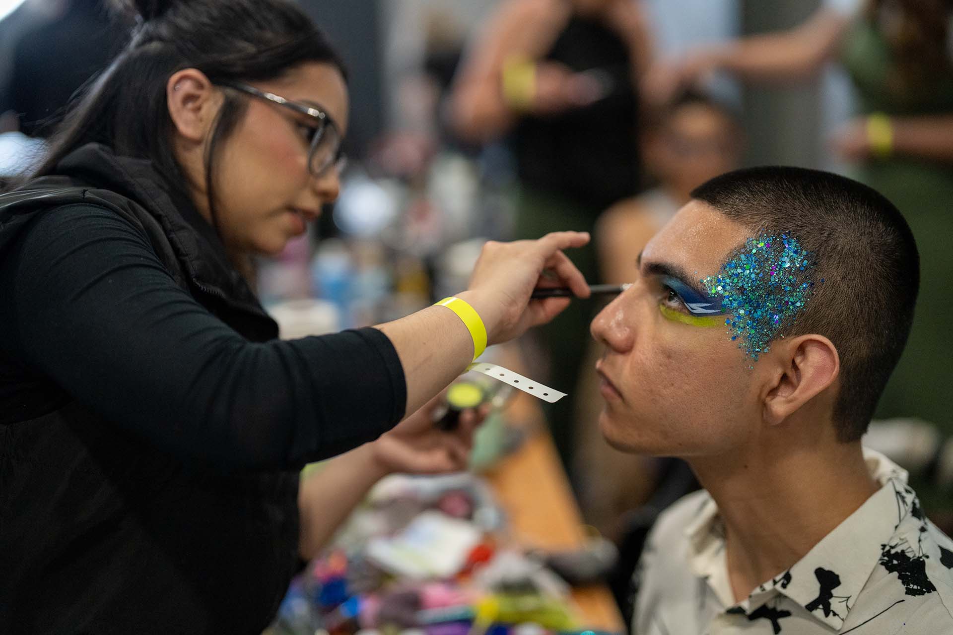 Backstage photo of a makeup artist applying makeup to a male model