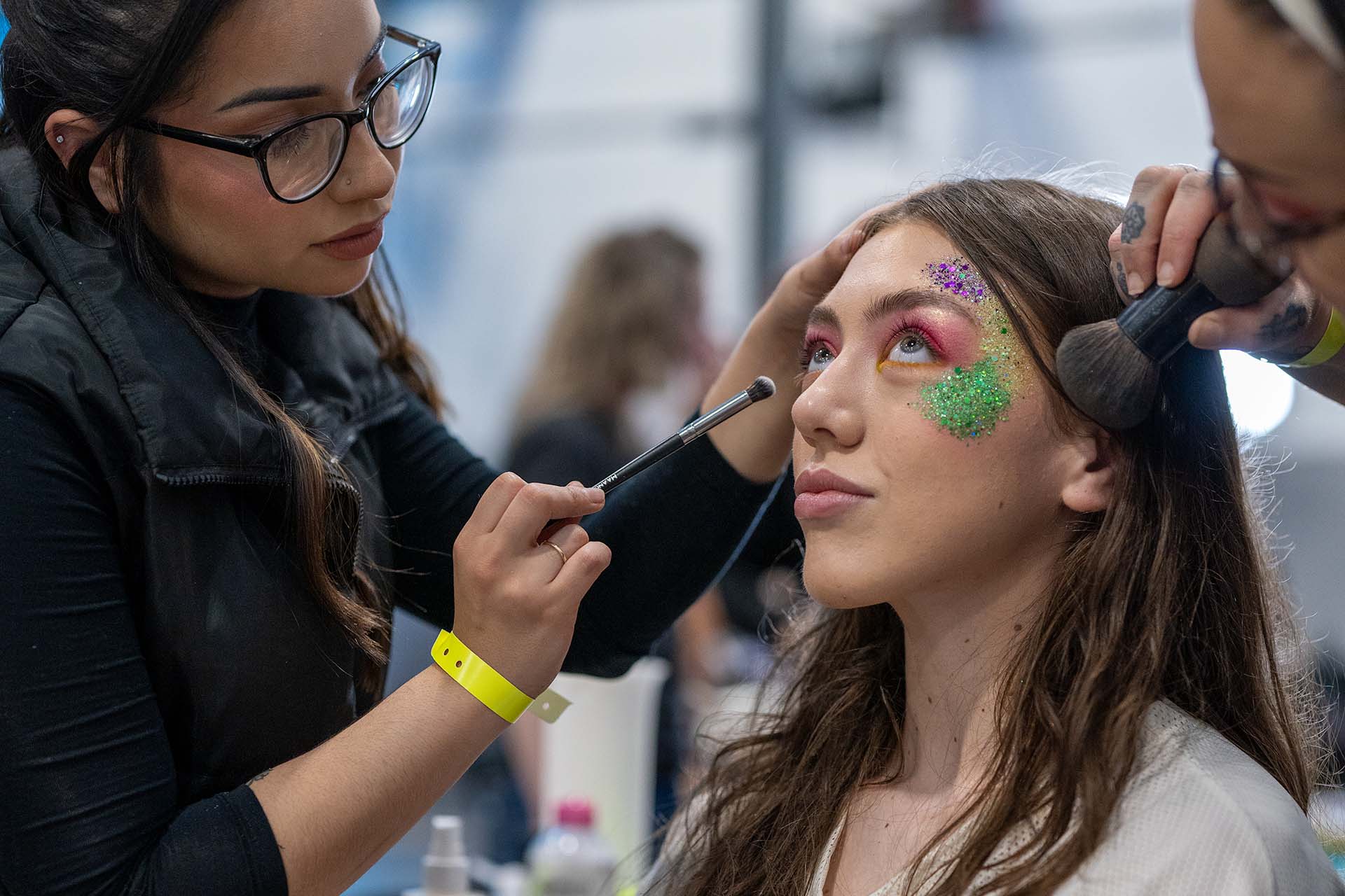 Backstage photo of a makeup artist applying green face makeup to a model