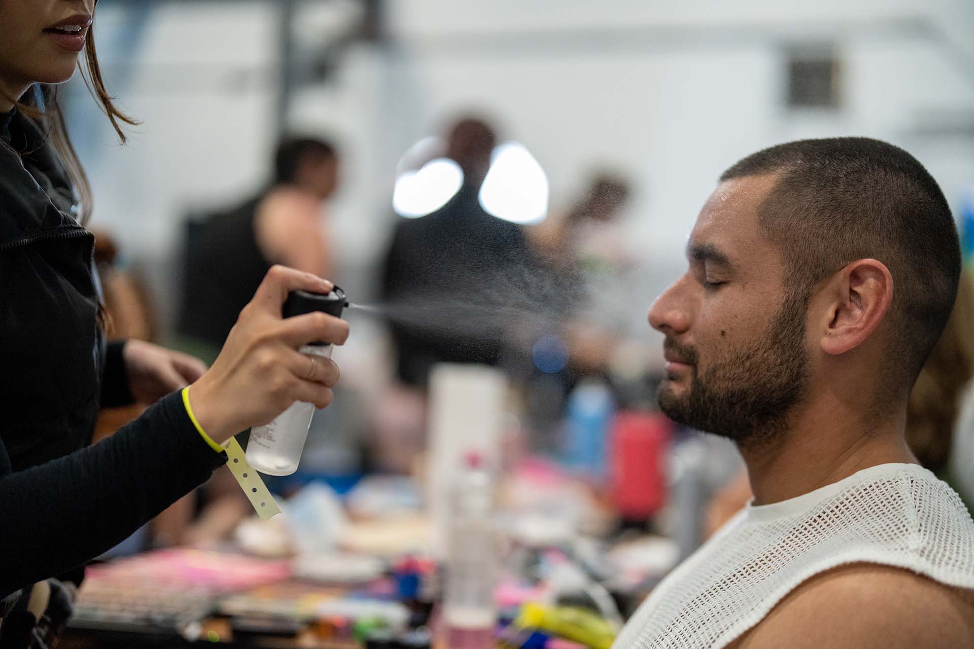 Backstage makeup artist spraying setting mist on a male model's face at Denver Fashion Week