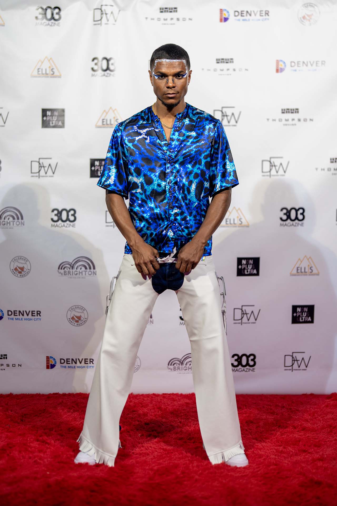 Model in a blue patterned shirt and white pants on the Denver Fashion Week red carpet step-and-repeat