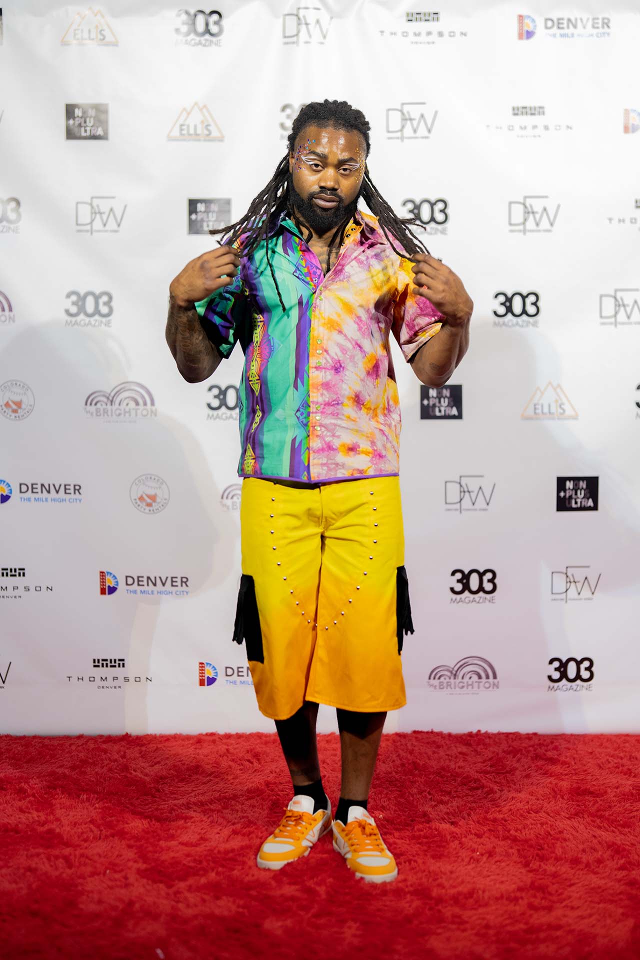 Model in a tie-dye shirt and yellow pants posing on the Denver Fashion Week red carpet