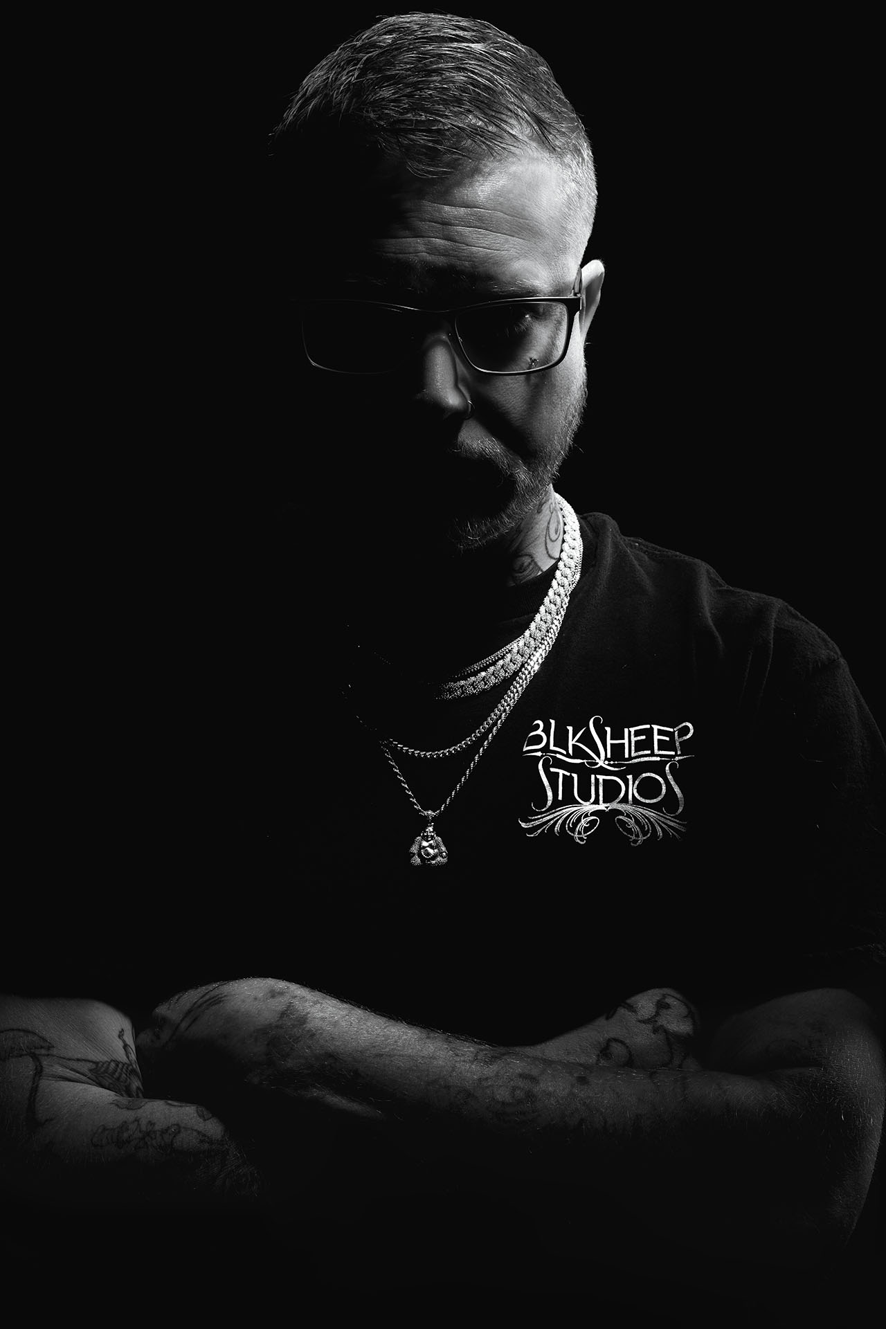 Dramatic black-and-white portrait of a tattoo artist wearing statement jewelry