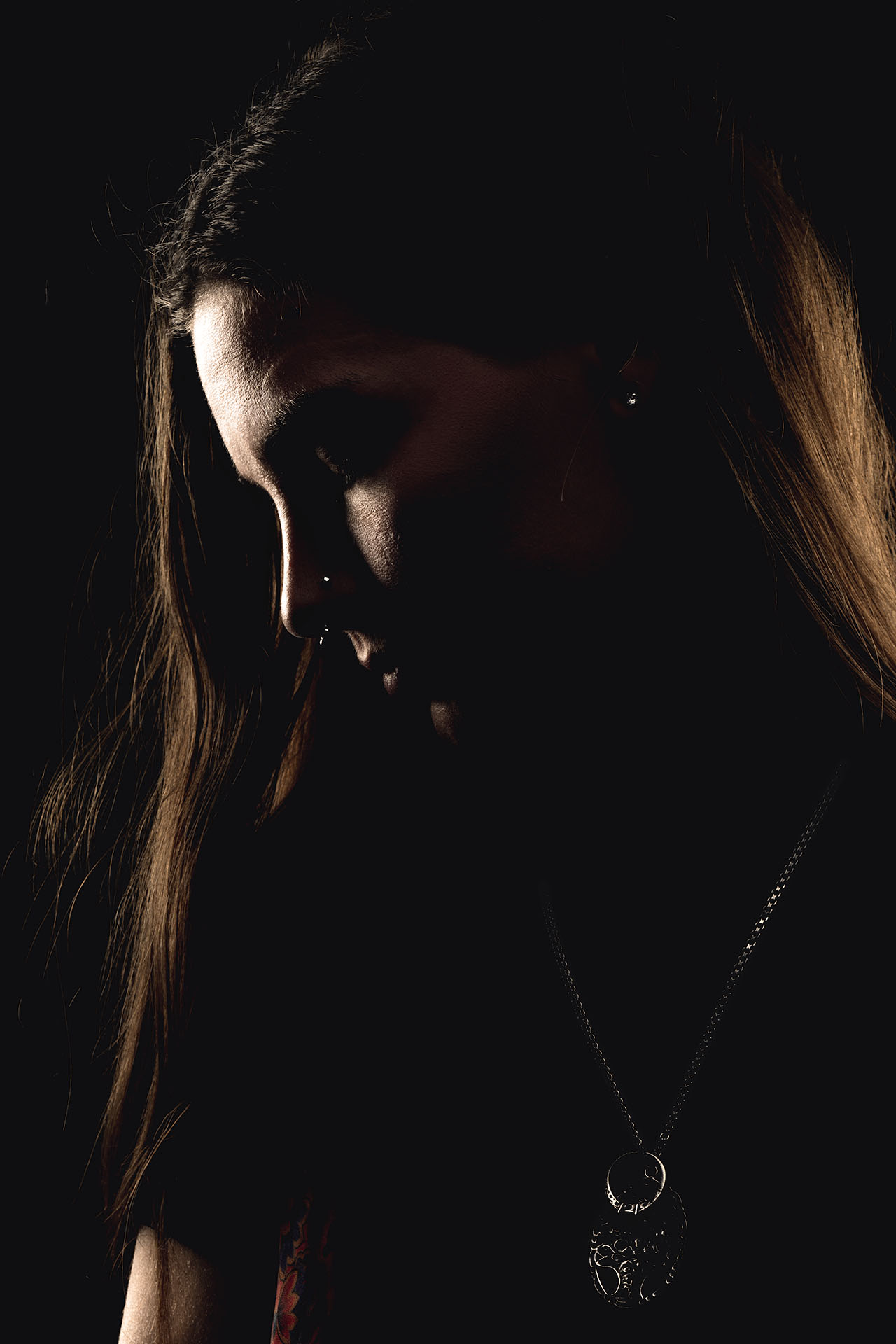 Dark moody portrait of a tattoo artist with hair partially covering her face, statement necklace visible