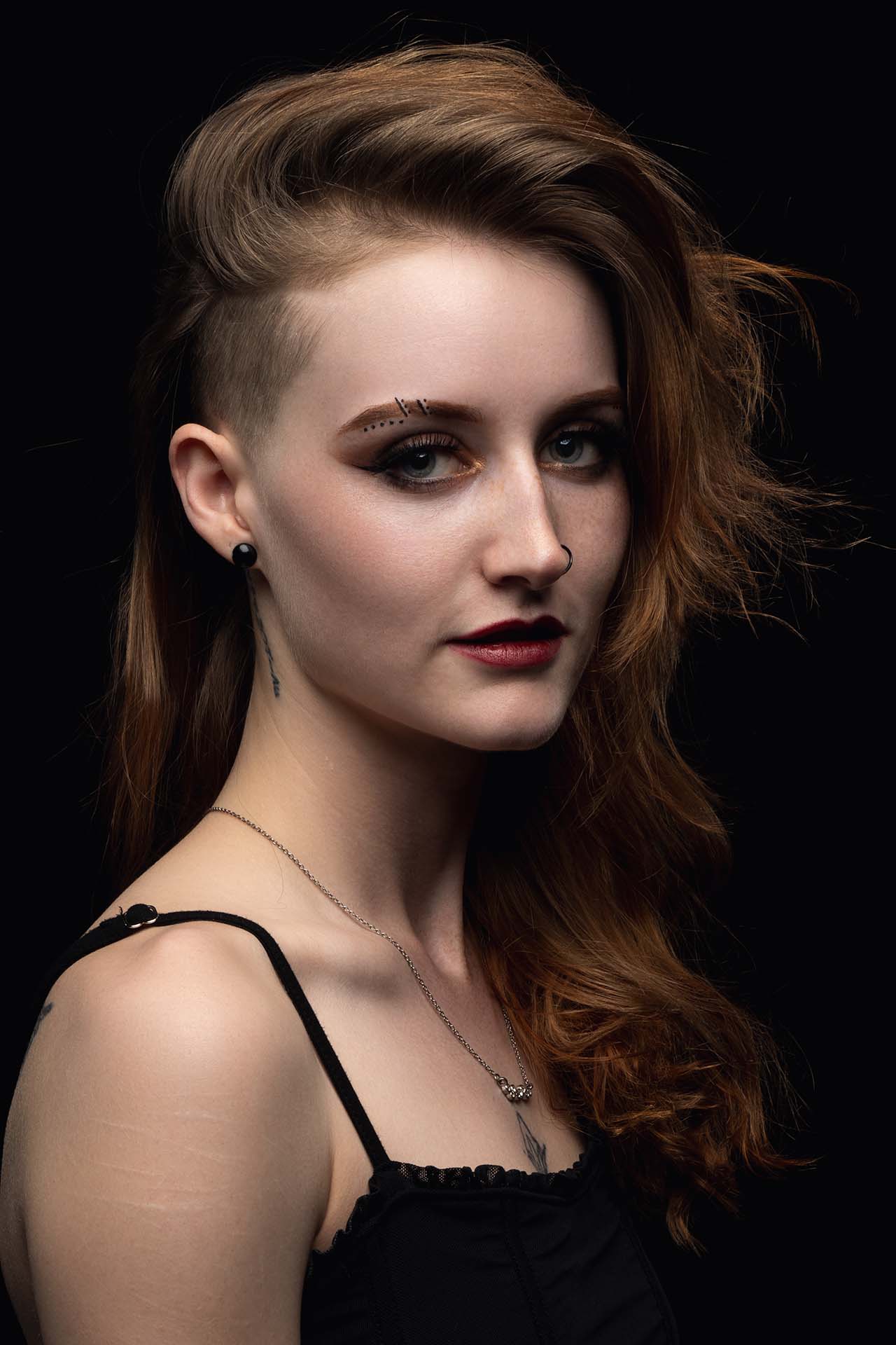 Beauty portrait of a tattoo artist with wavy auburn hair and dramatic dark makeup