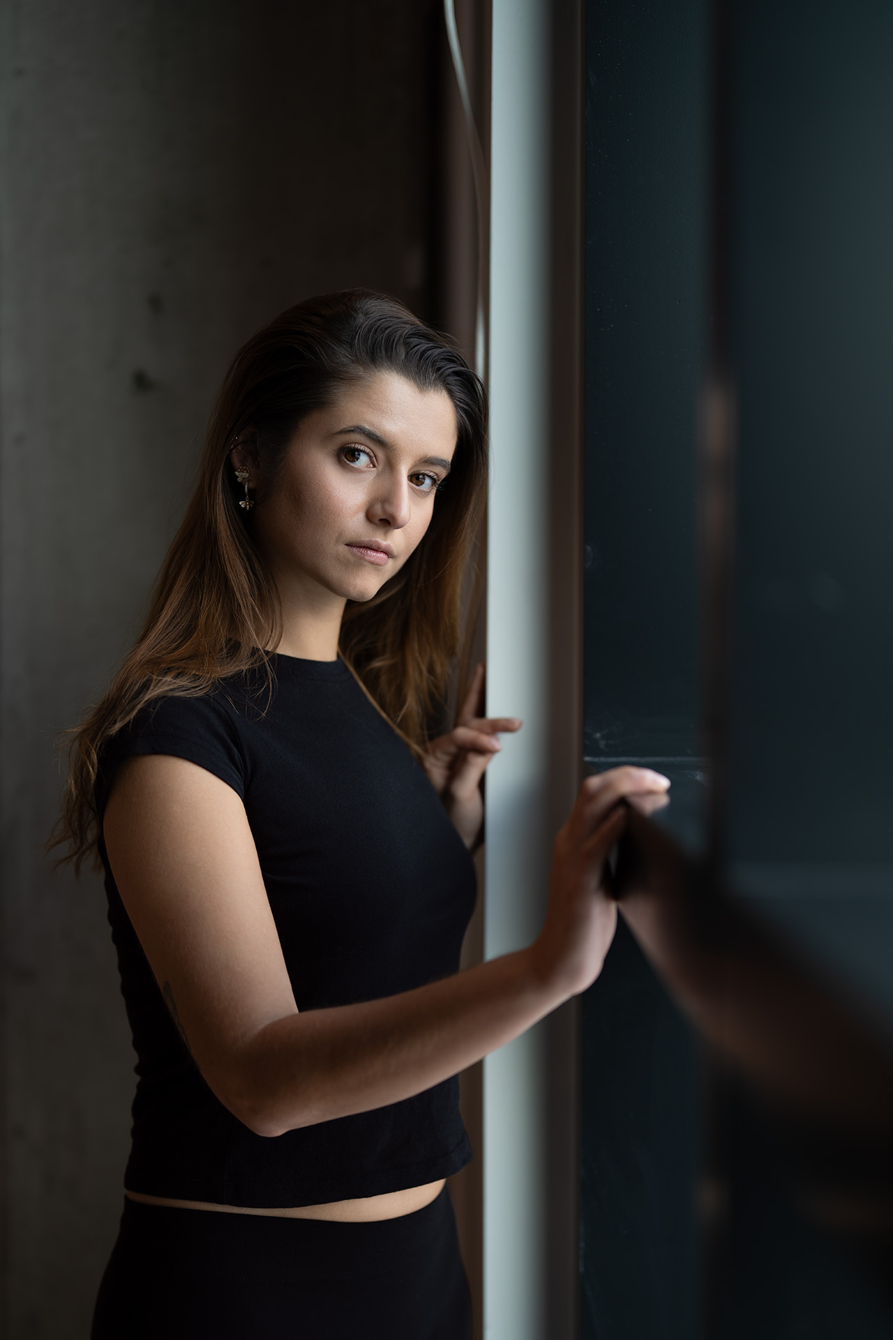 Portrait of a model in a black top leaning against a window, moody natural light