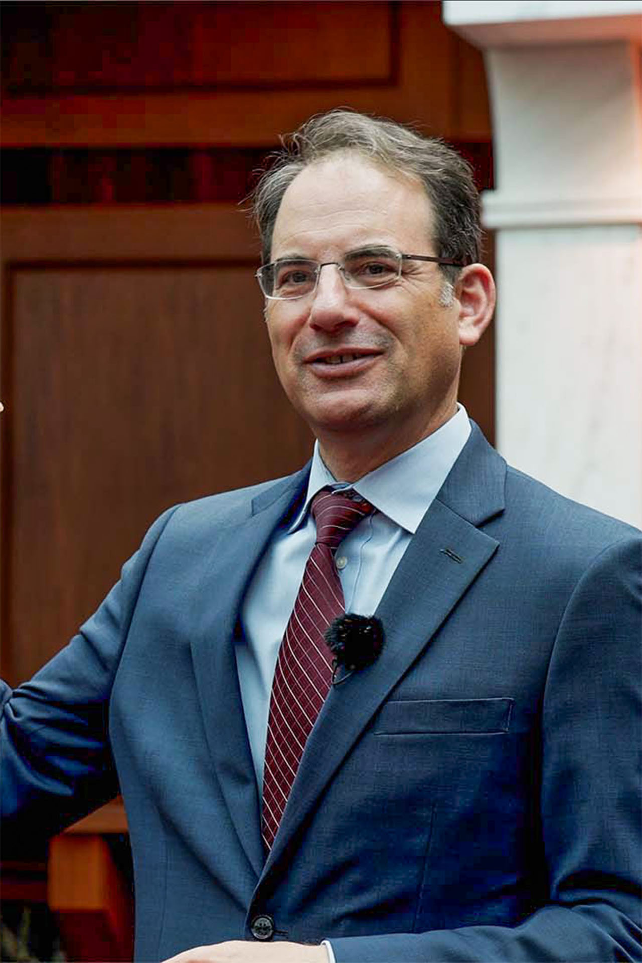 Portrait of Colorado Attorney General Phil Weiser in a blue suit and red tie, smiling, at a formal event
