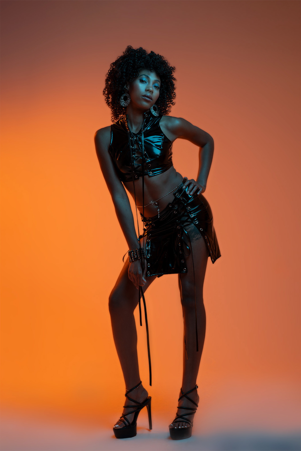 Model in a black leather outfit posing dramatically against a bold orange background
