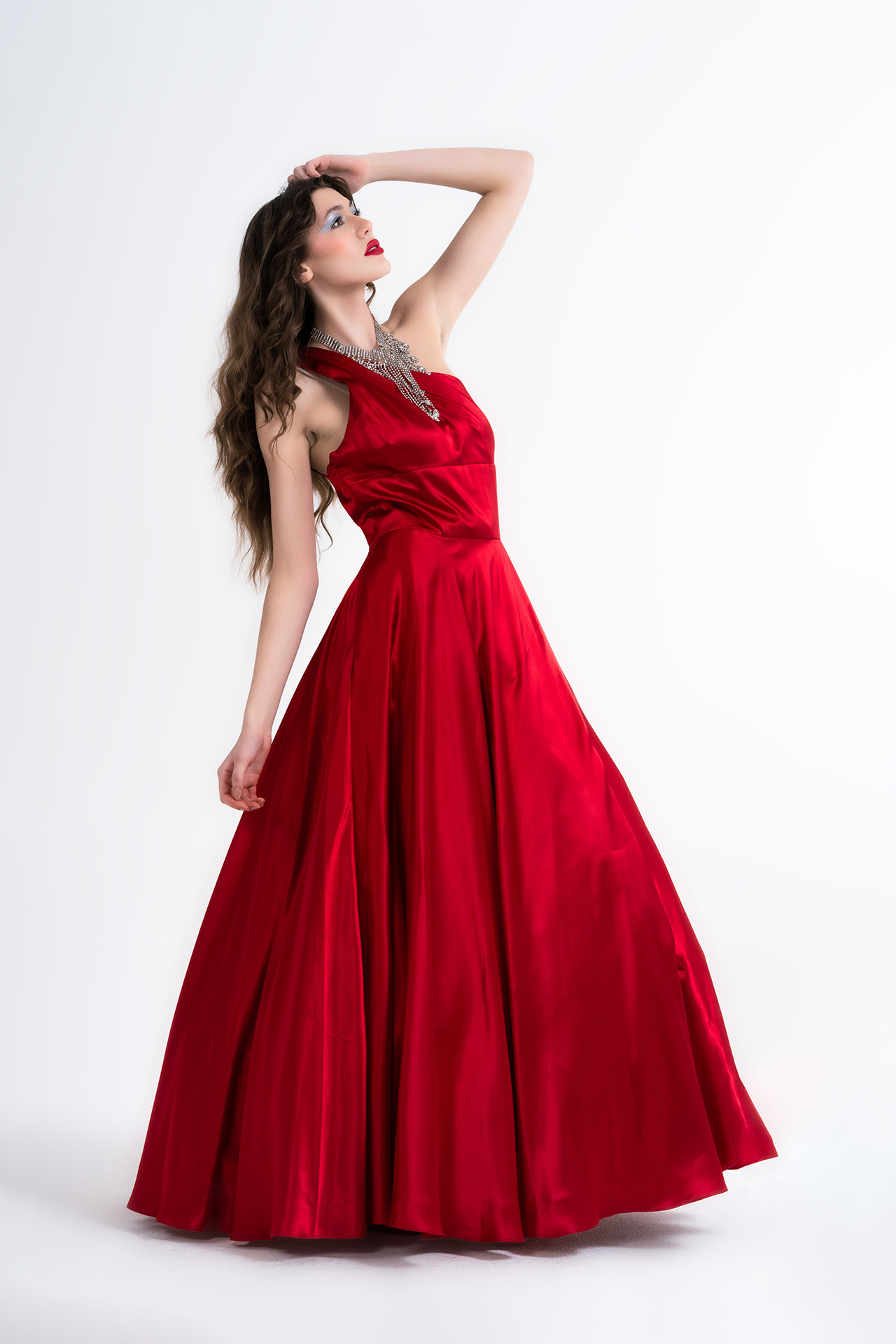 Model in a flowing red evening gown, dramatic pose with hand above the head, studio photography