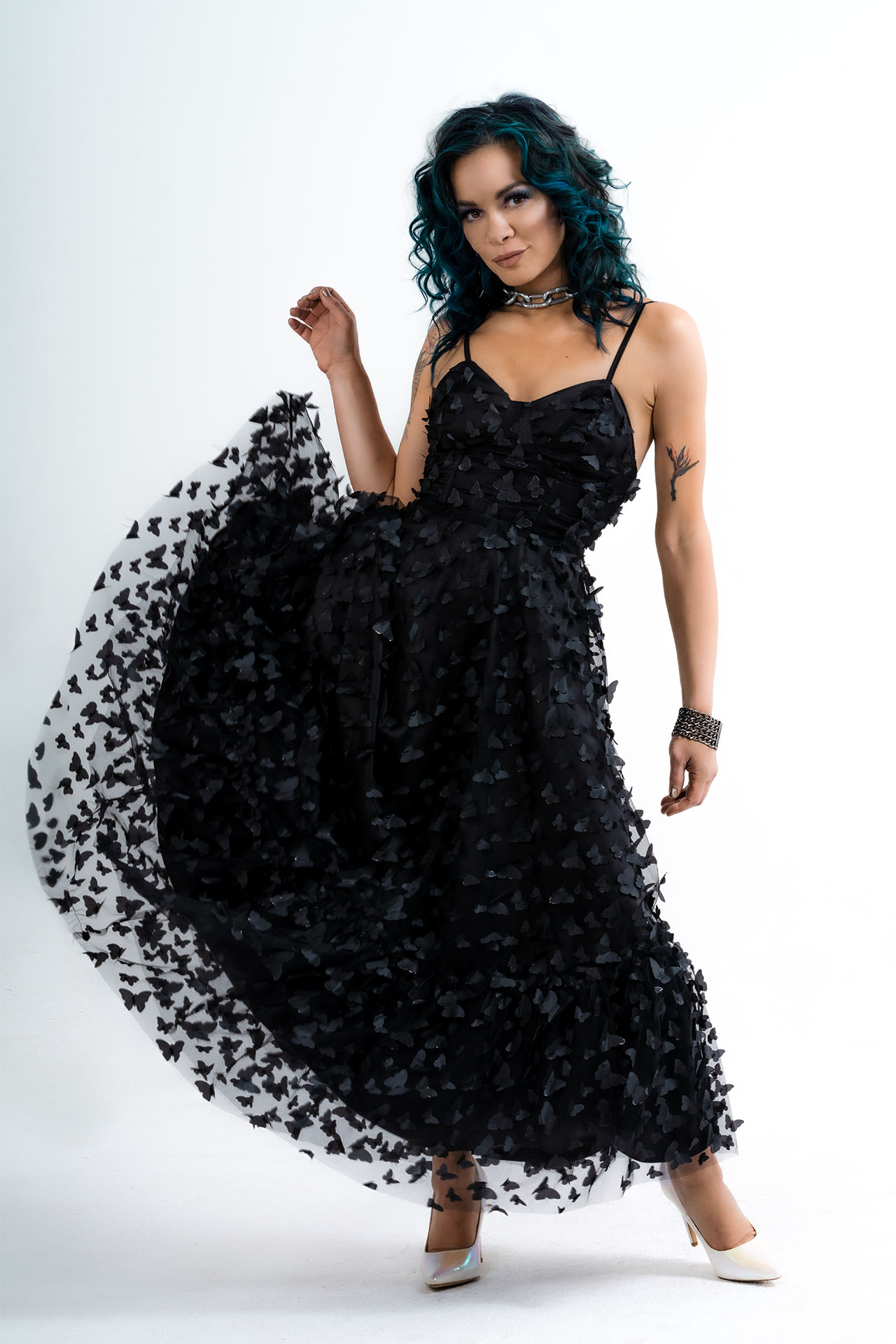 Model with teal hair in a black butterfly-print tulle dress, standing pose with skirt swept out