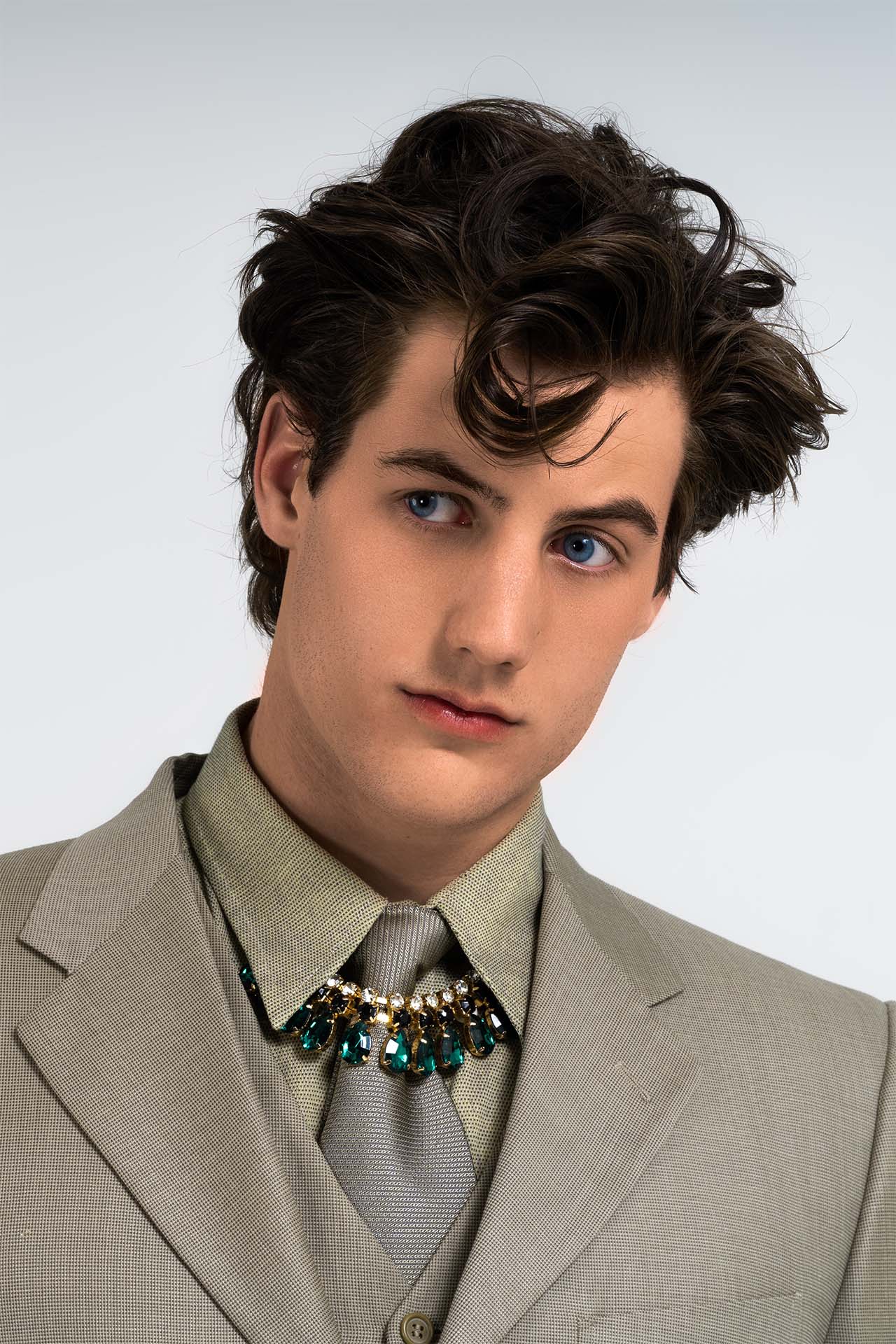 Male model in a tan suit with statement jewelry, formal editorial portrait, wavy hairstyle