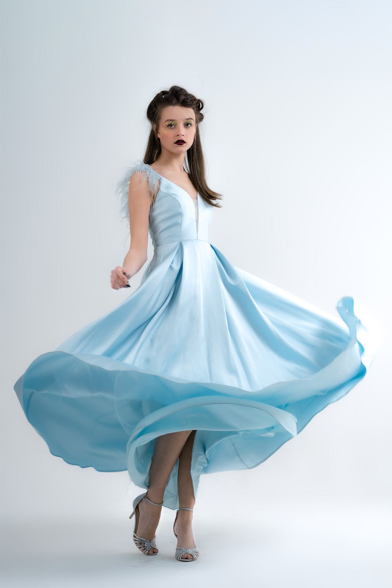 Model in a flowing light blue gown captured mid-twirl, dynamic studio fashion photography