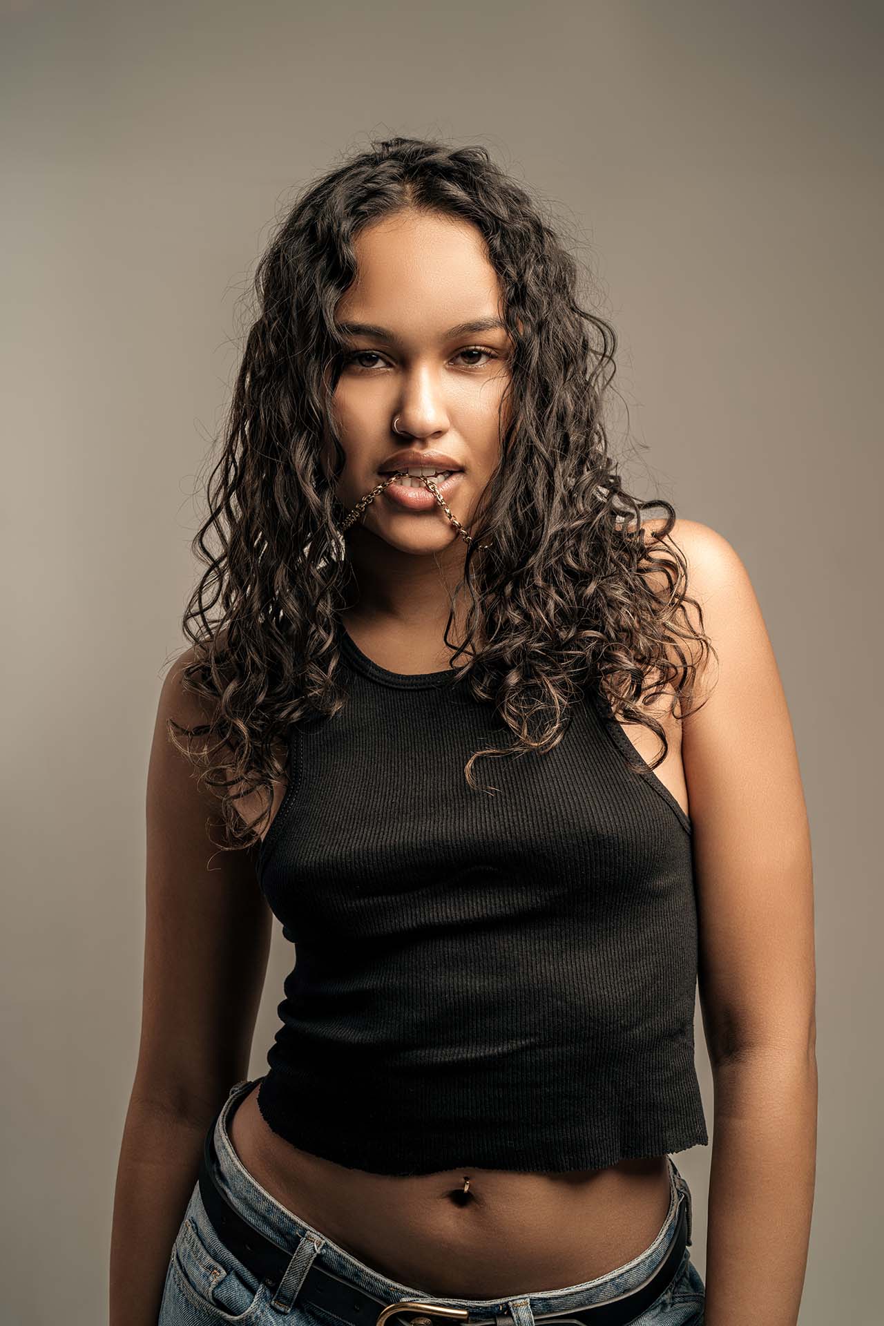 Beauty portrait of a model with curly hair in a black top, warm-toned studio background