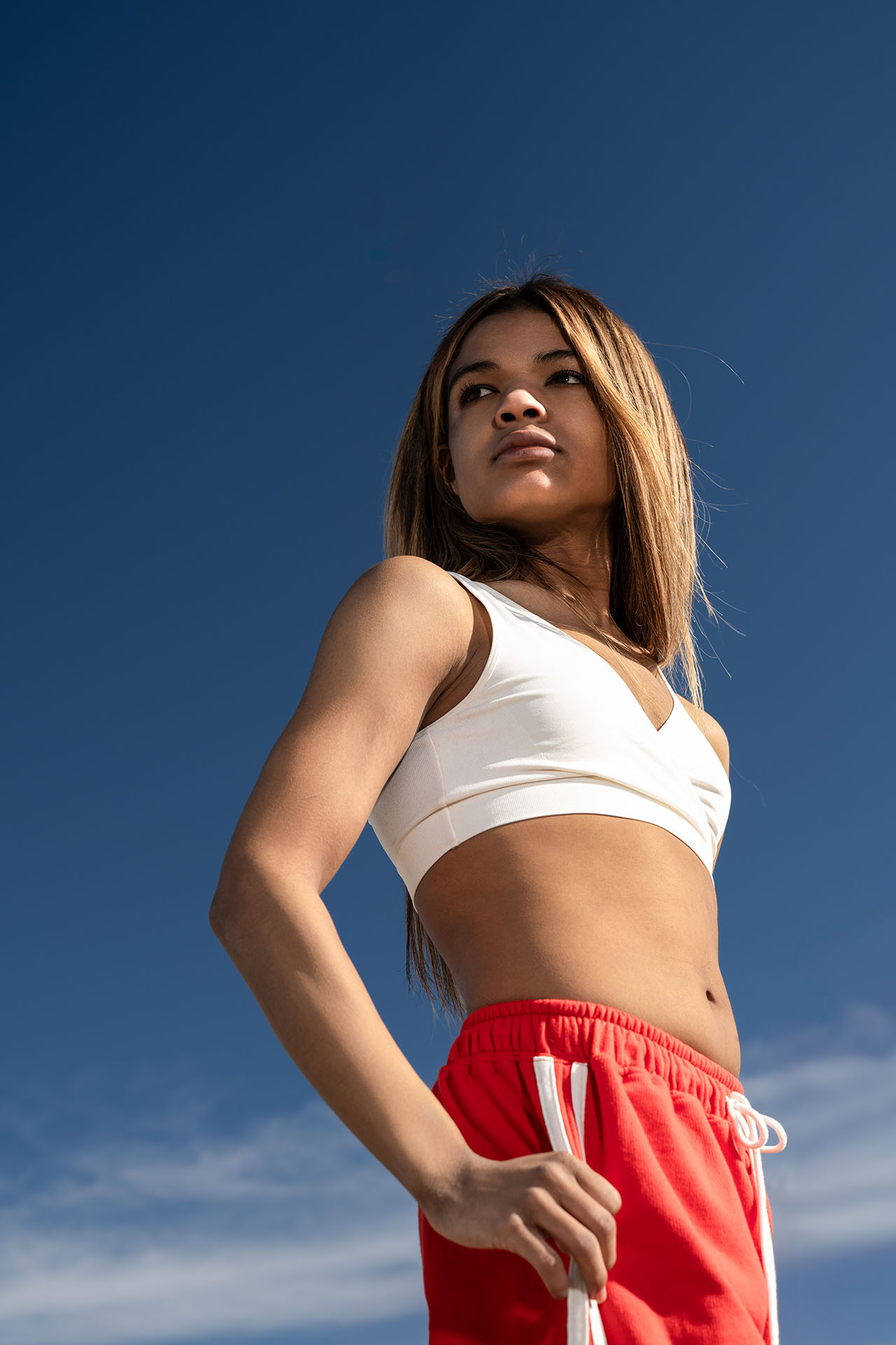 Model in a white crop top and red track pants posing against a clear blue sky, Denver fashion photography
