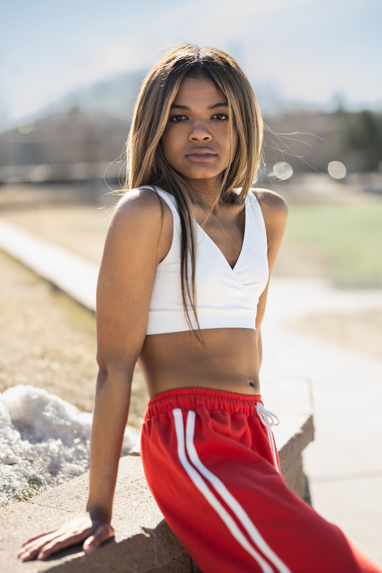 Model in a white crop top and red track pants posing outdoors on a walking path, Aurora & Denver fashion photography