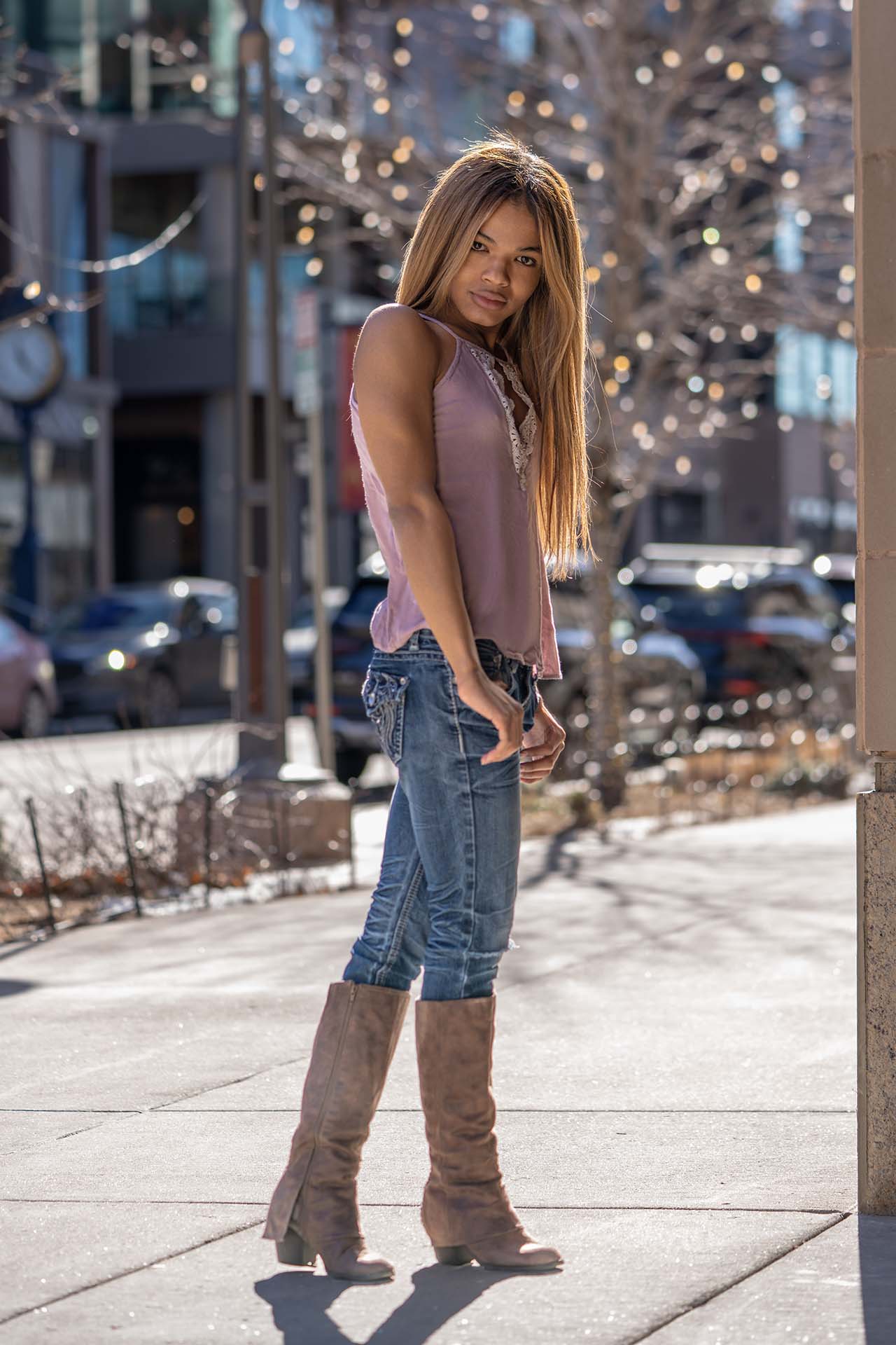 Model walking down a Denver street in denim and boots under tree lights, morning fashion photography