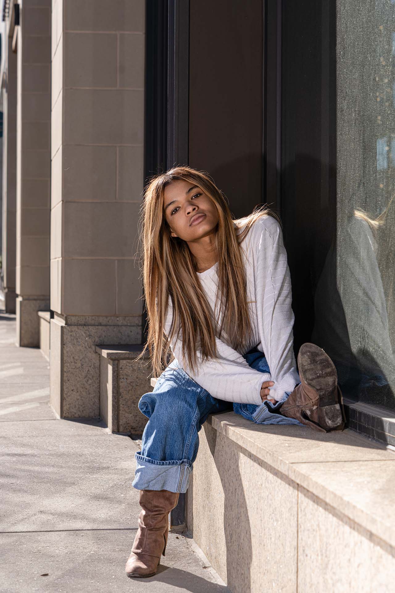 Model seated on a stone window ledge in jeans and boots, urban architecture backdrop, Denver fashion photography