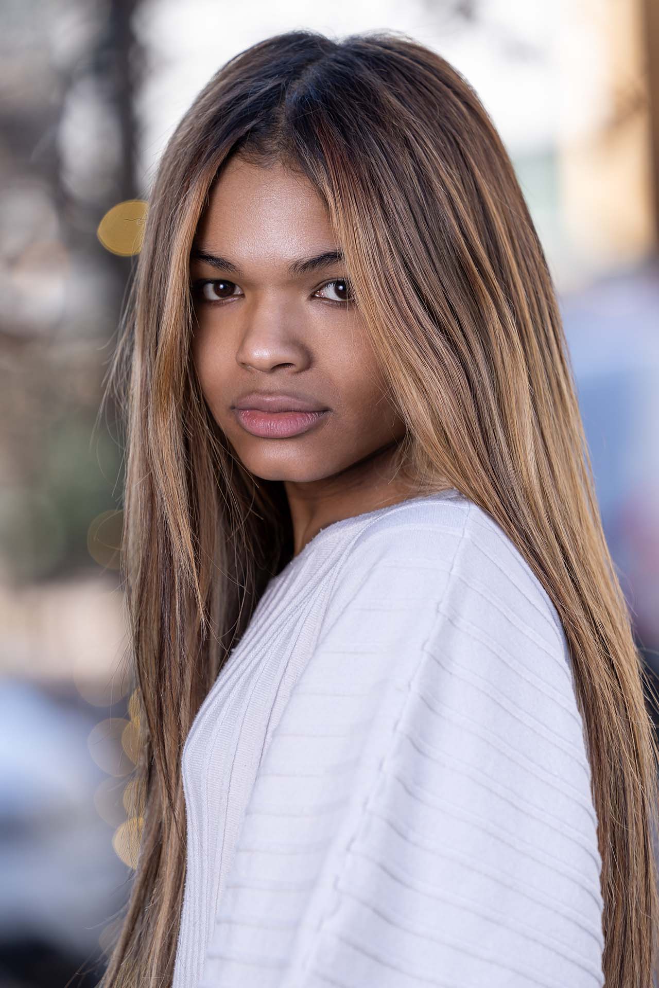 Close-up portrait of a model in a white striped top with wavy hair, urban background