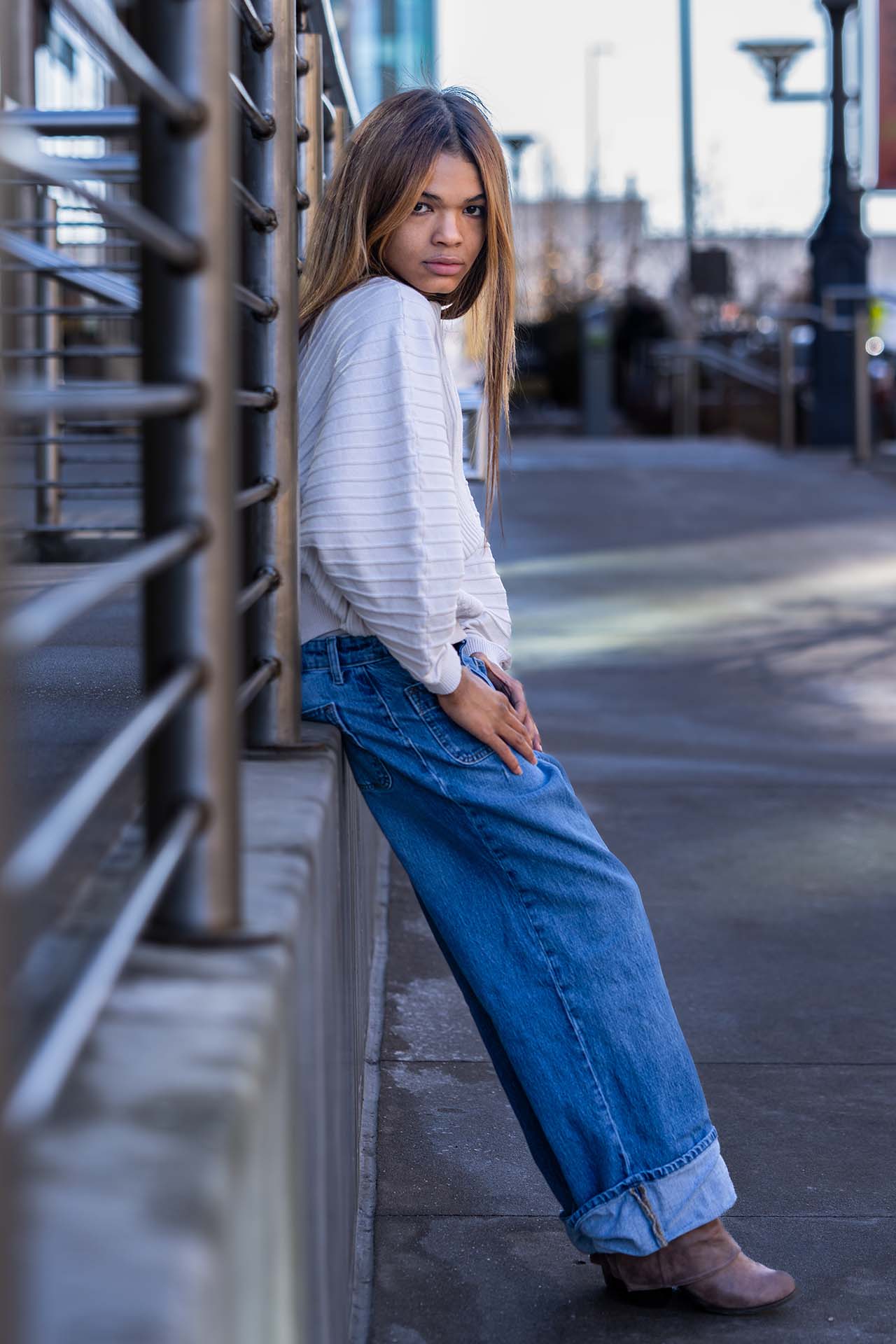 Model in denim leaning against an urban railing, full-length street fashion photography