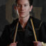 College graduate Austin in cap and gown with gold honor cords, portrait orientation studio photo