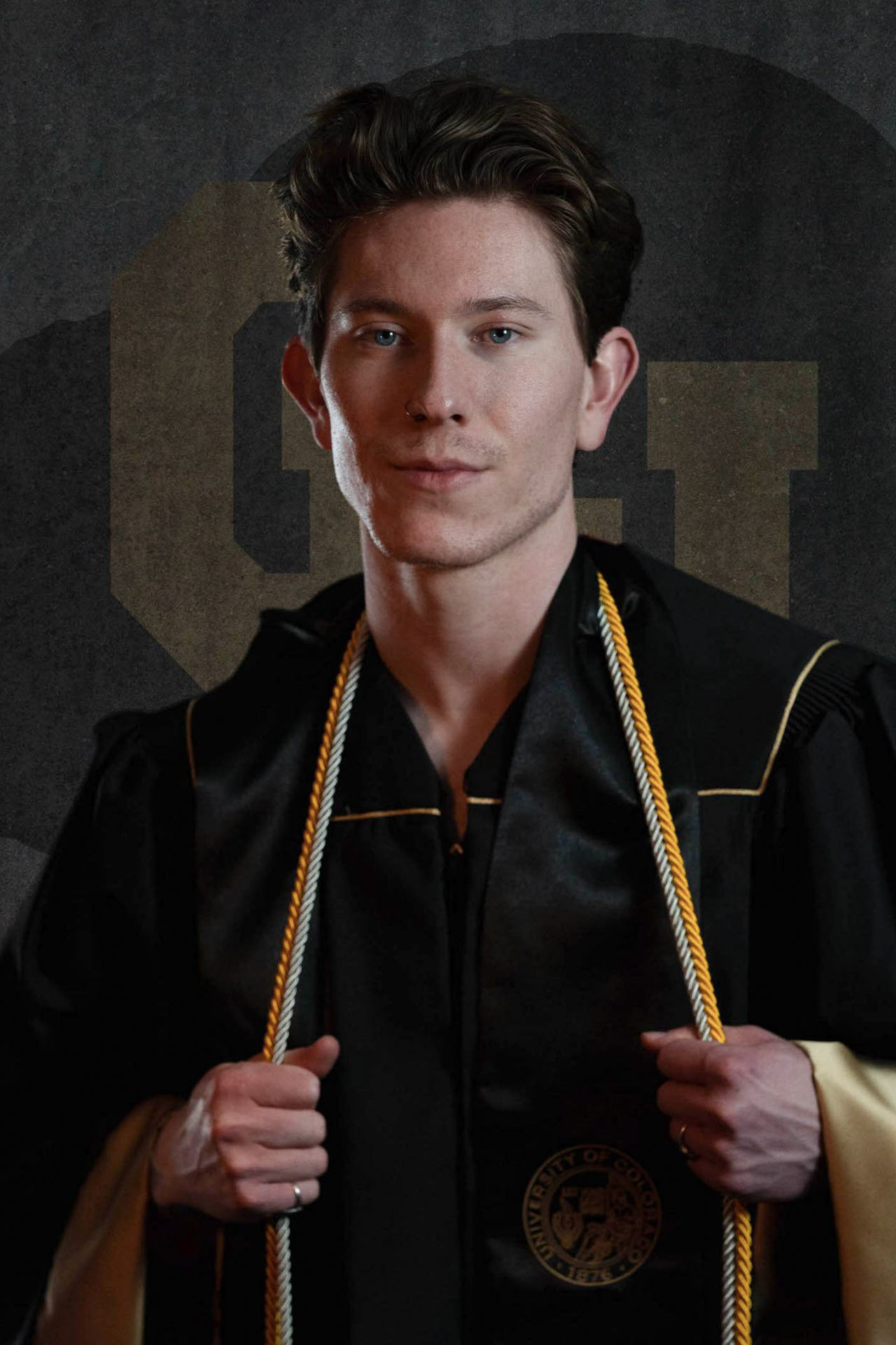 College graduate Austin in cap and gown with gold honor cords, portrait orientation studio photo