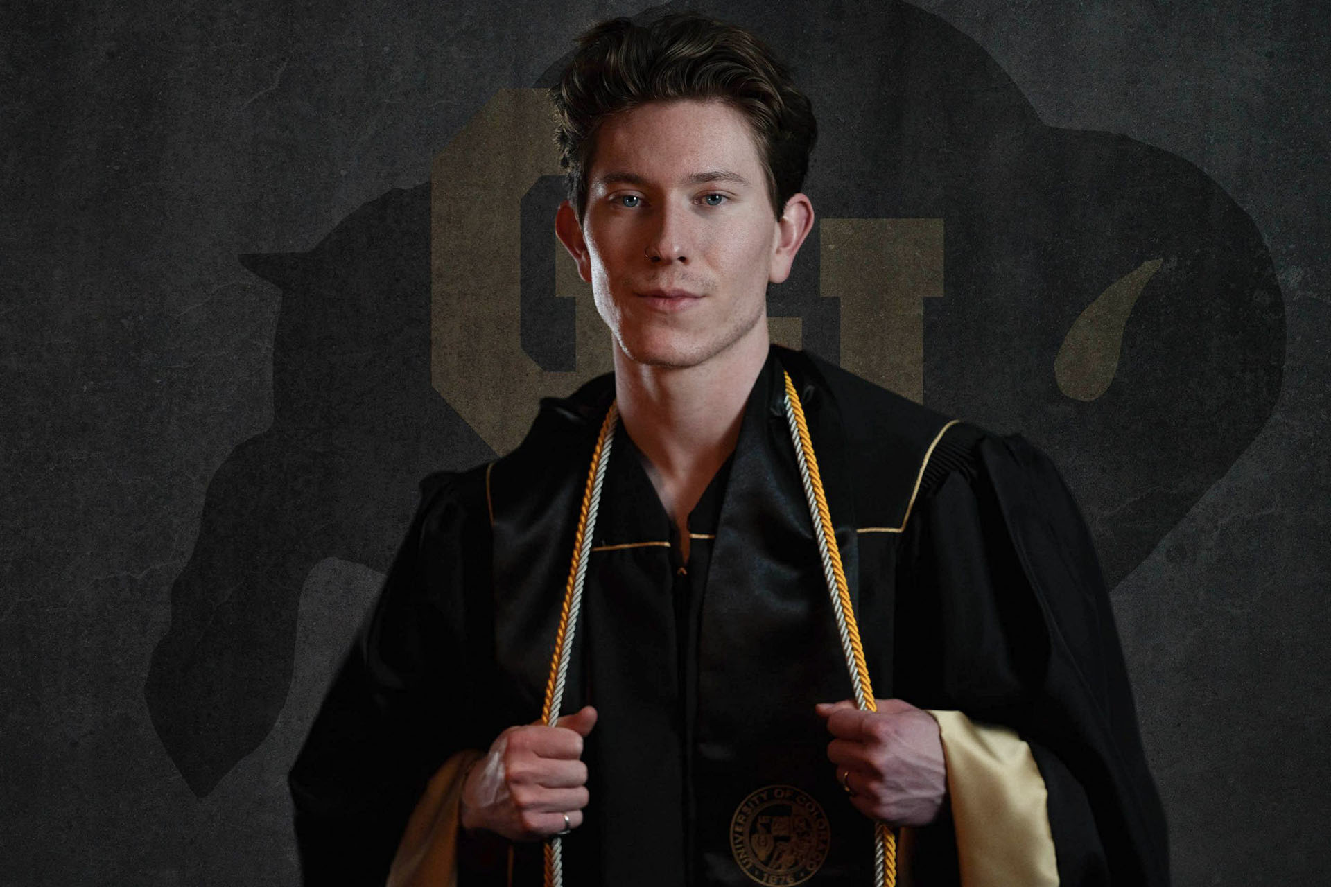 College graduate Austin in cap and gown with gold honor cords, landscape orientation studio photo