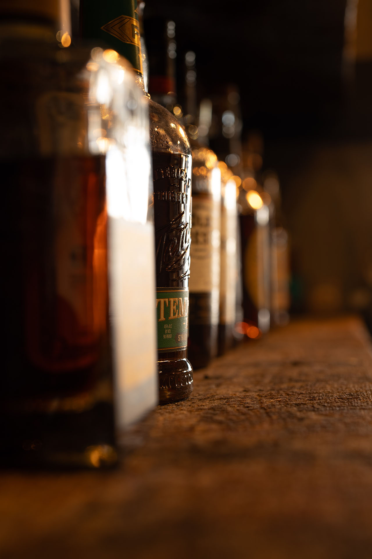 Rows of bottles along a dimly lit bar, moody bar interior photography