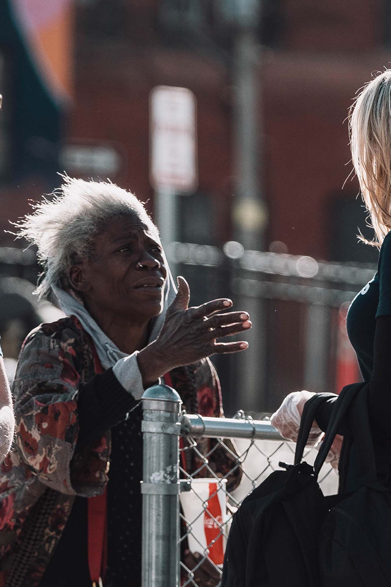 Unhoused woman speaking with Be Kind volunteers, vertical crop, Denver