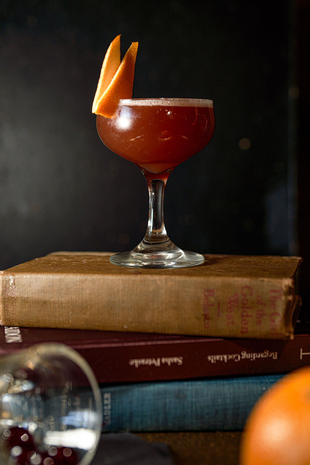 Blood and Sand cocktail with an orange twist, styled on antique books with a magnifying glass, at Pretty Neat Bar