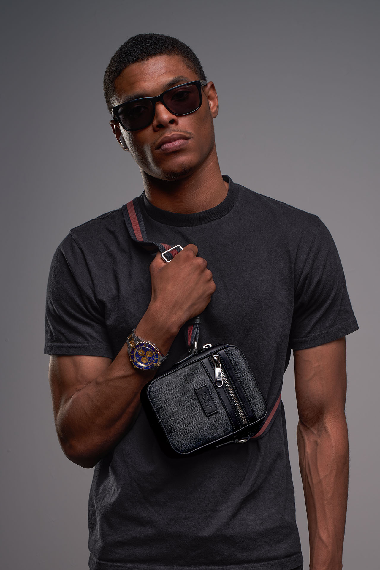 Male model in sunglasses and a black t-shirt with a crossbody bag, studio menswear photography