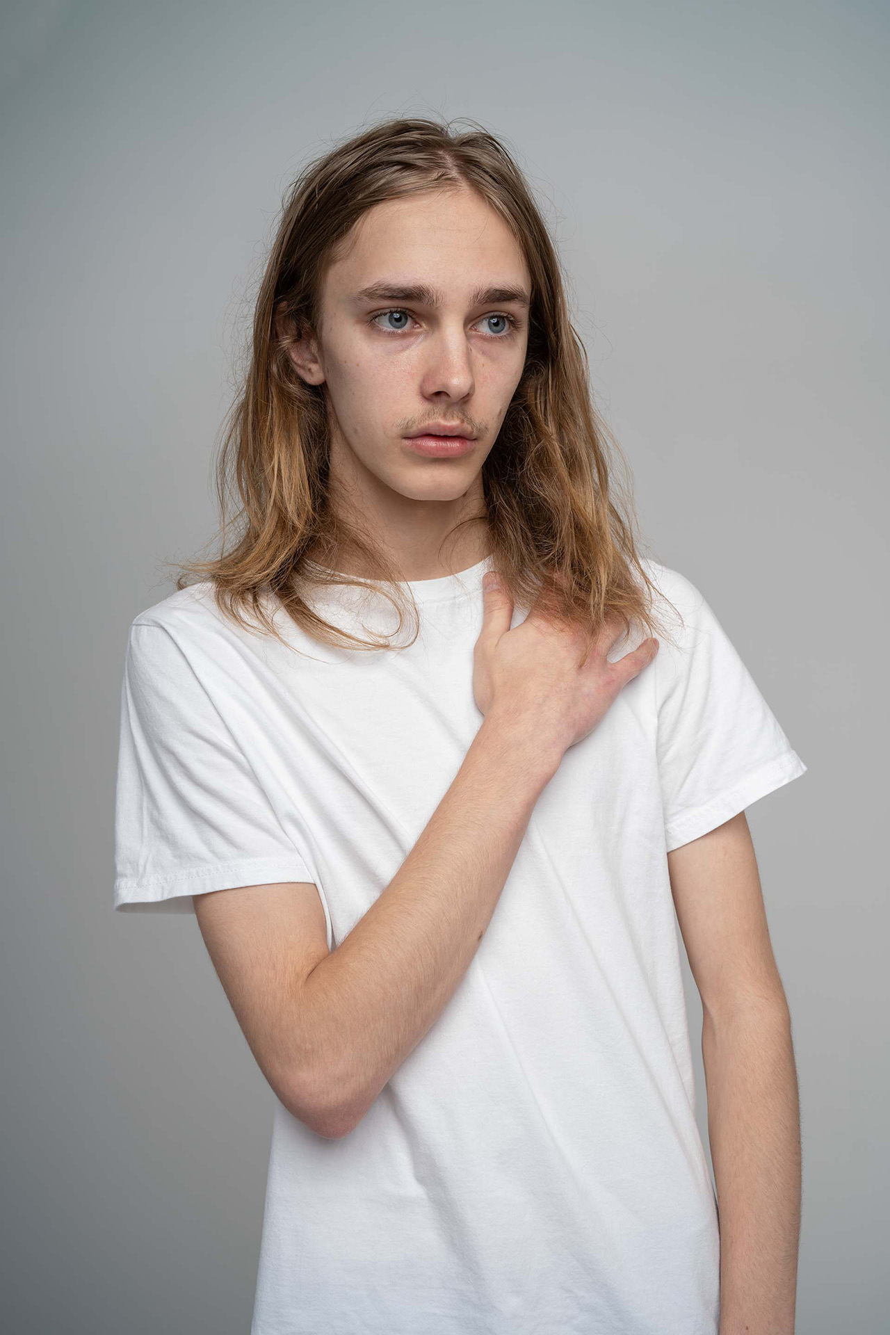 Male model portfolio digital with long hair and hand resting on chest, white t-shirt