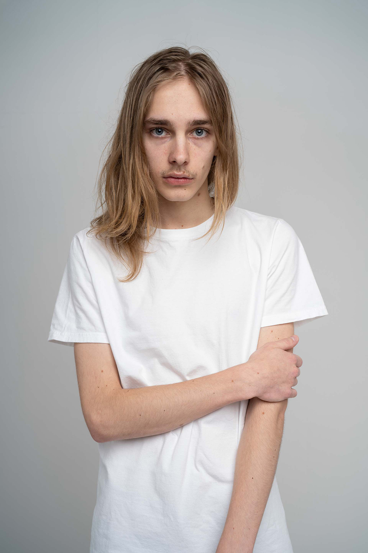 Male model portfolio digital with arm crossed, white t-shirt, neutral studio background