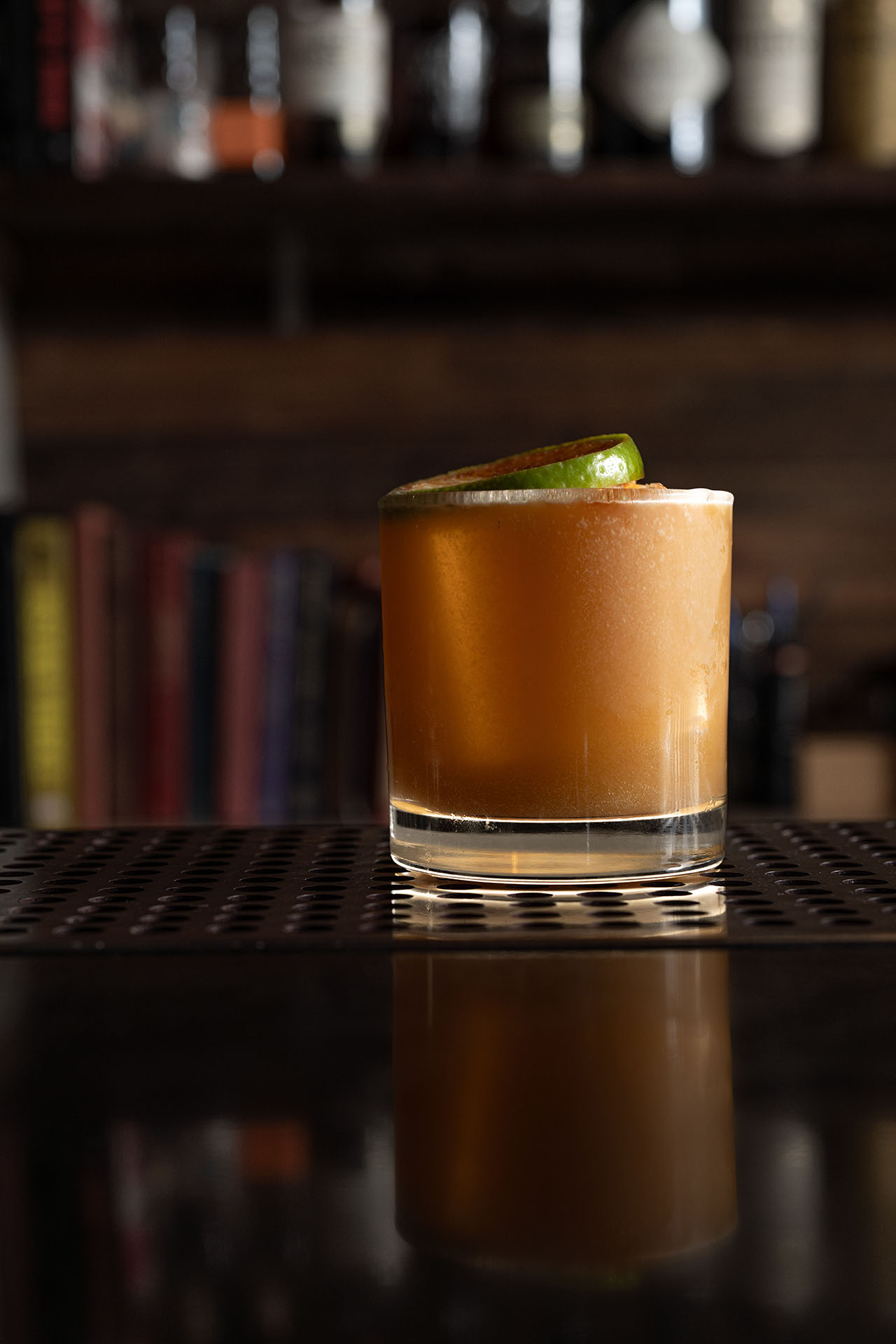 Down with the Ship cocktail garnished with lime, styled against a bookshelf, at Pretty Neat Bar