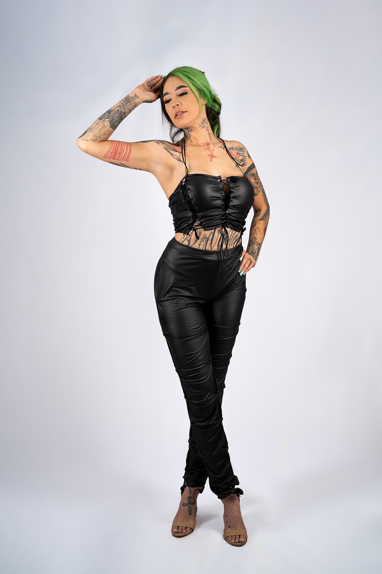 Full-body model portfolio digital with green hair and tattoos, arm raised, black leather outfit