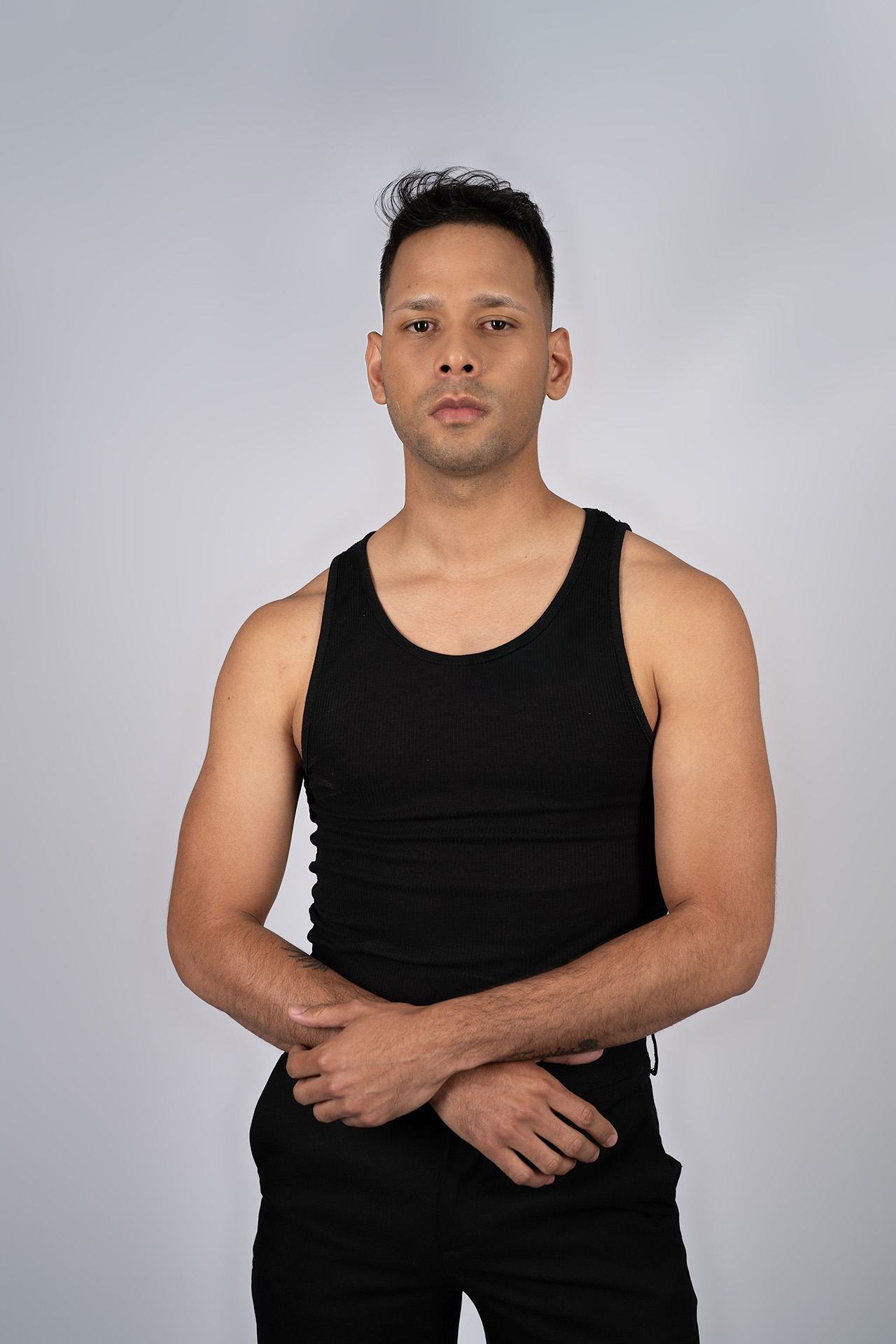 Half-body male model portfolio digital in a black tank top, arms crossed, gray studio background
