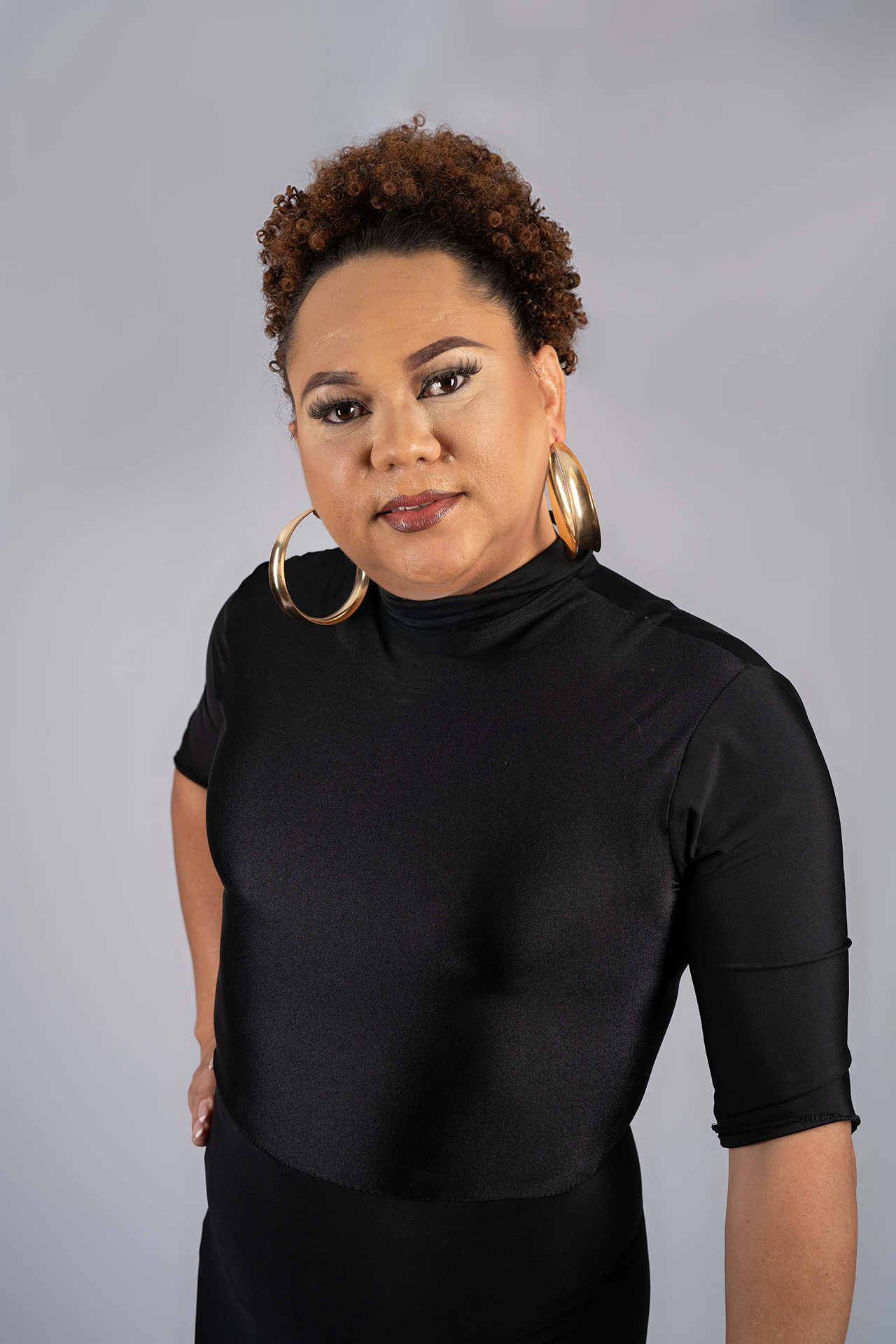 Model portfolio digital with curly hair and hoop earrings in a black turtleneck top, hand on hip
