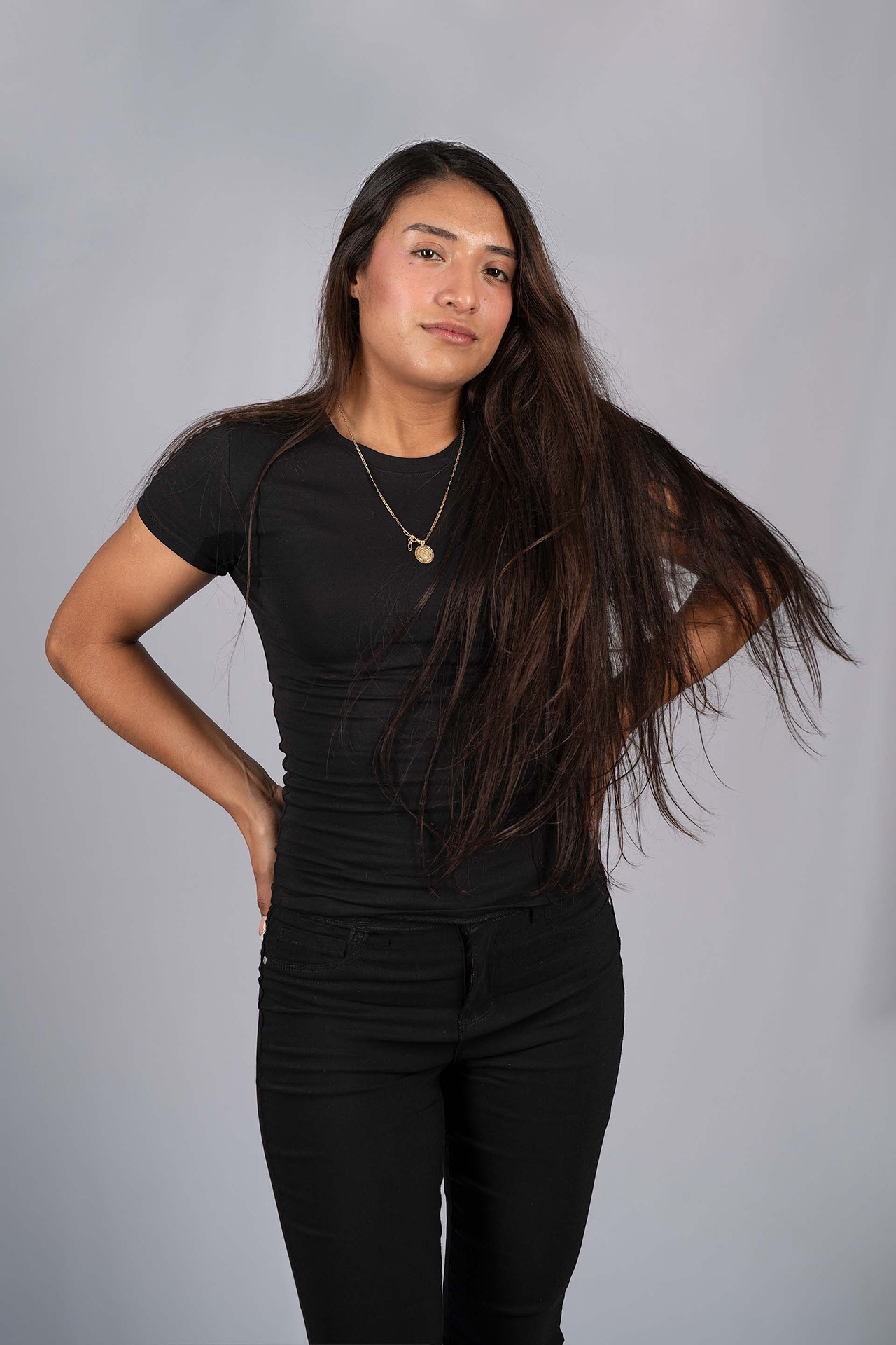 Knees-up model portfolio digital with long hair, black t-shirt and pants, hand on hip