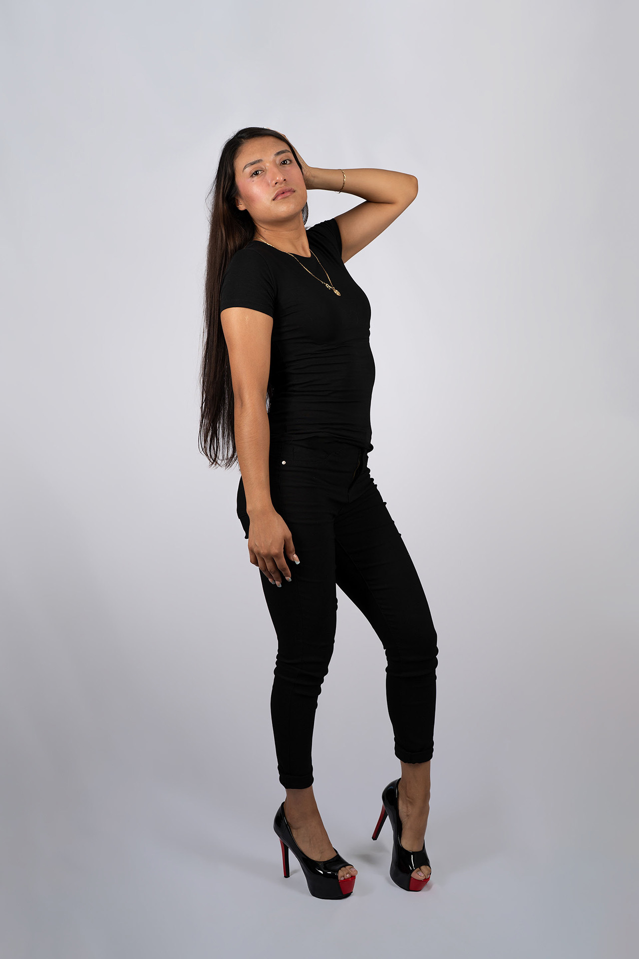 Full-body model portfolio digital with hand near her head, playful pose, black outfit and heels
