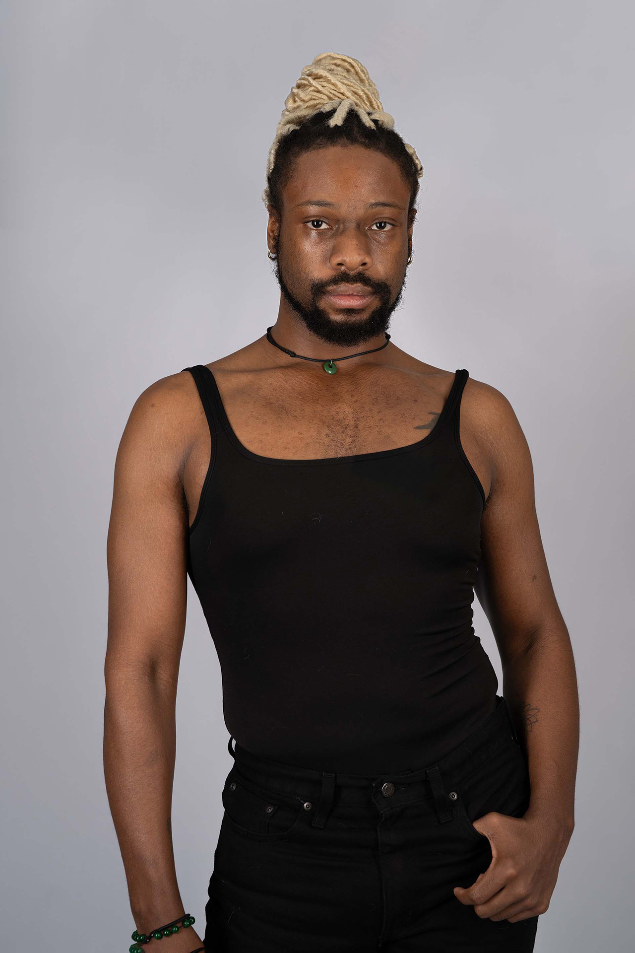 Male model portfolio digital with hair in a top bun, black tank top and jeans