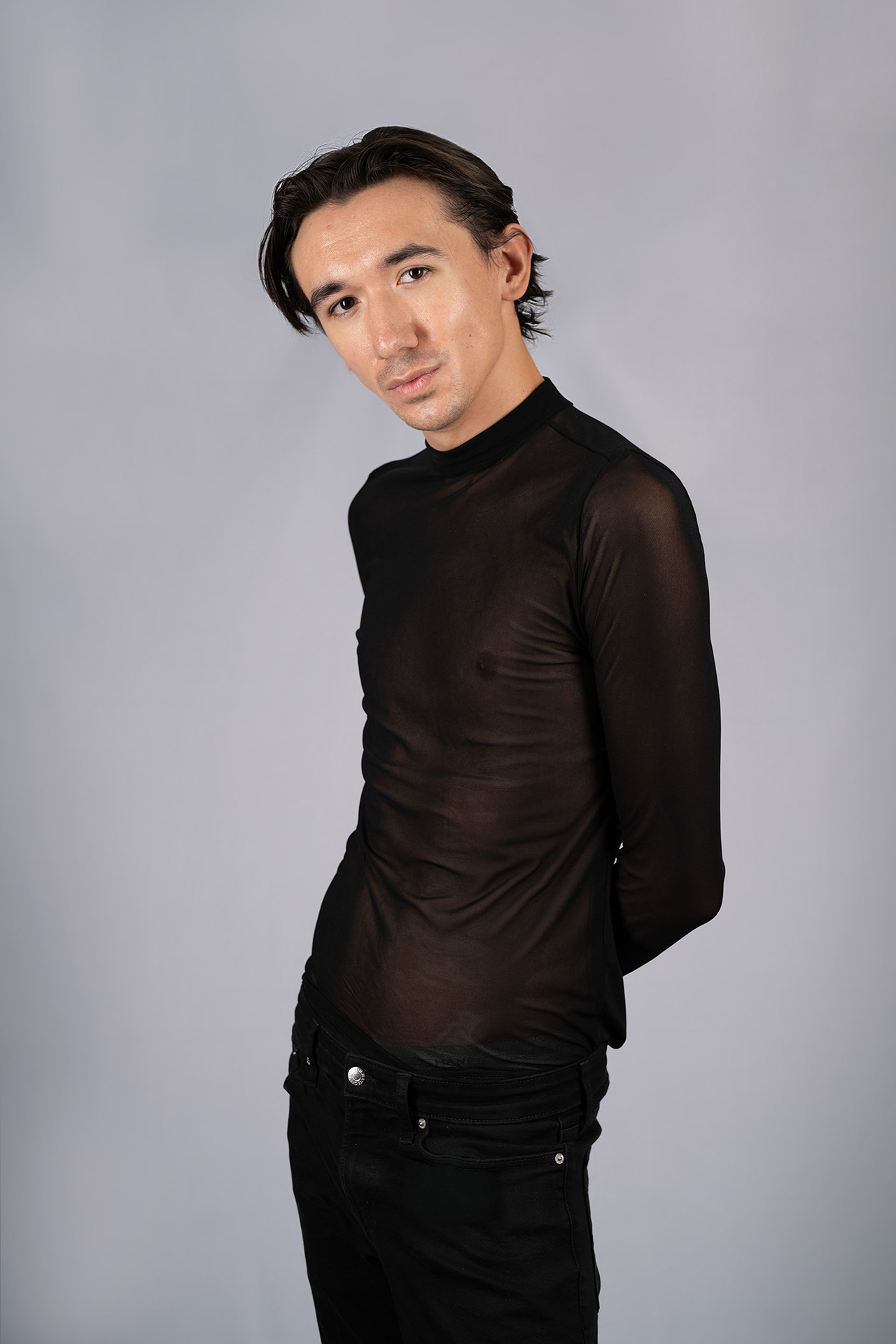 Male model portfolio digital in a sheer black mesh top and black pants, side pose