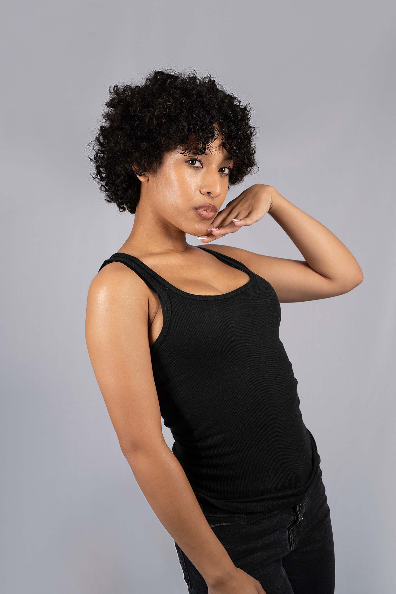 Model portfolio digital with curly hair, black tank top, hand resting near the face