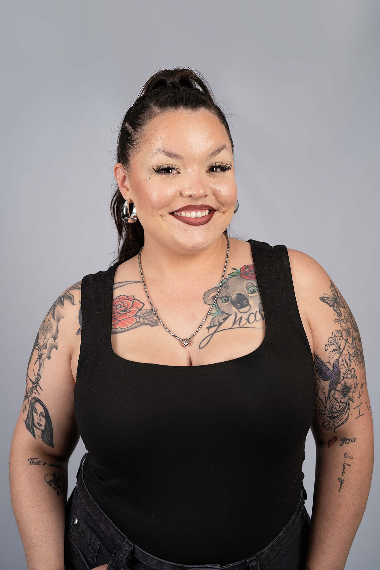 Model portfolio digital with tattoos, smiling, black tank top, gray studio background