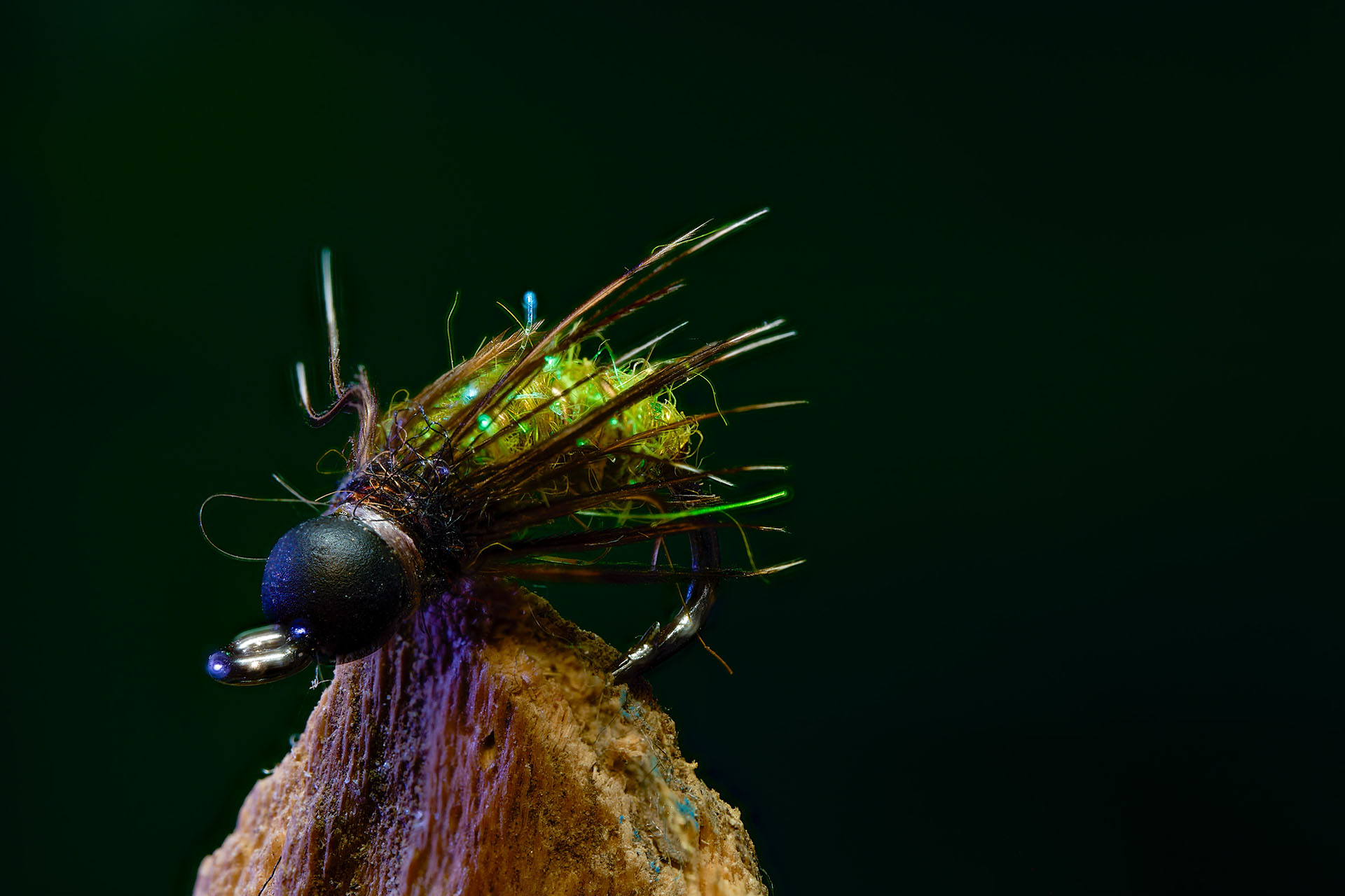 Macro product photo of a hand-tied fishing fly on a wood perch against a dark background