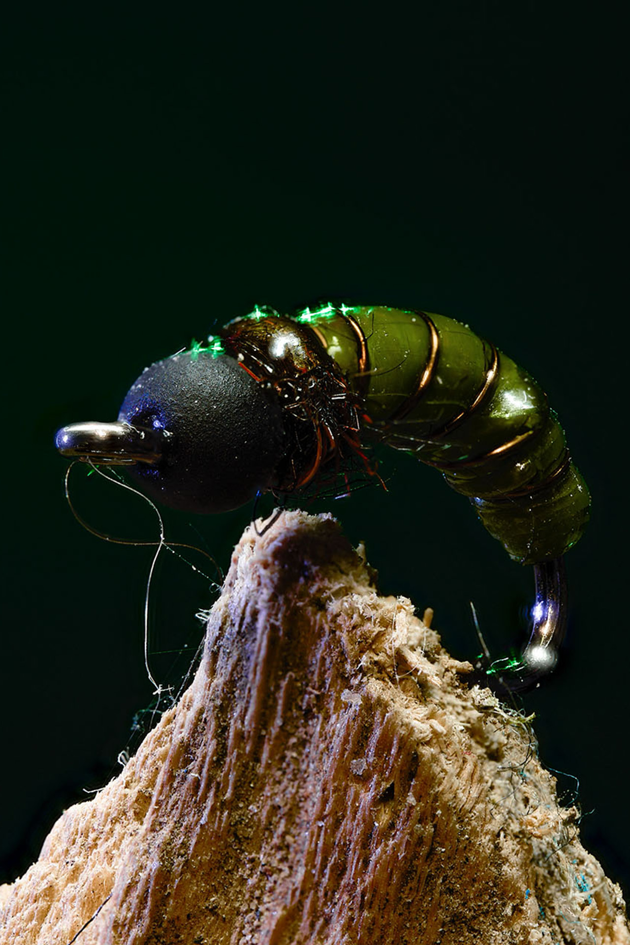 Close-up macro photo of an iridescent green fly-tying fly mounted on a wood perch