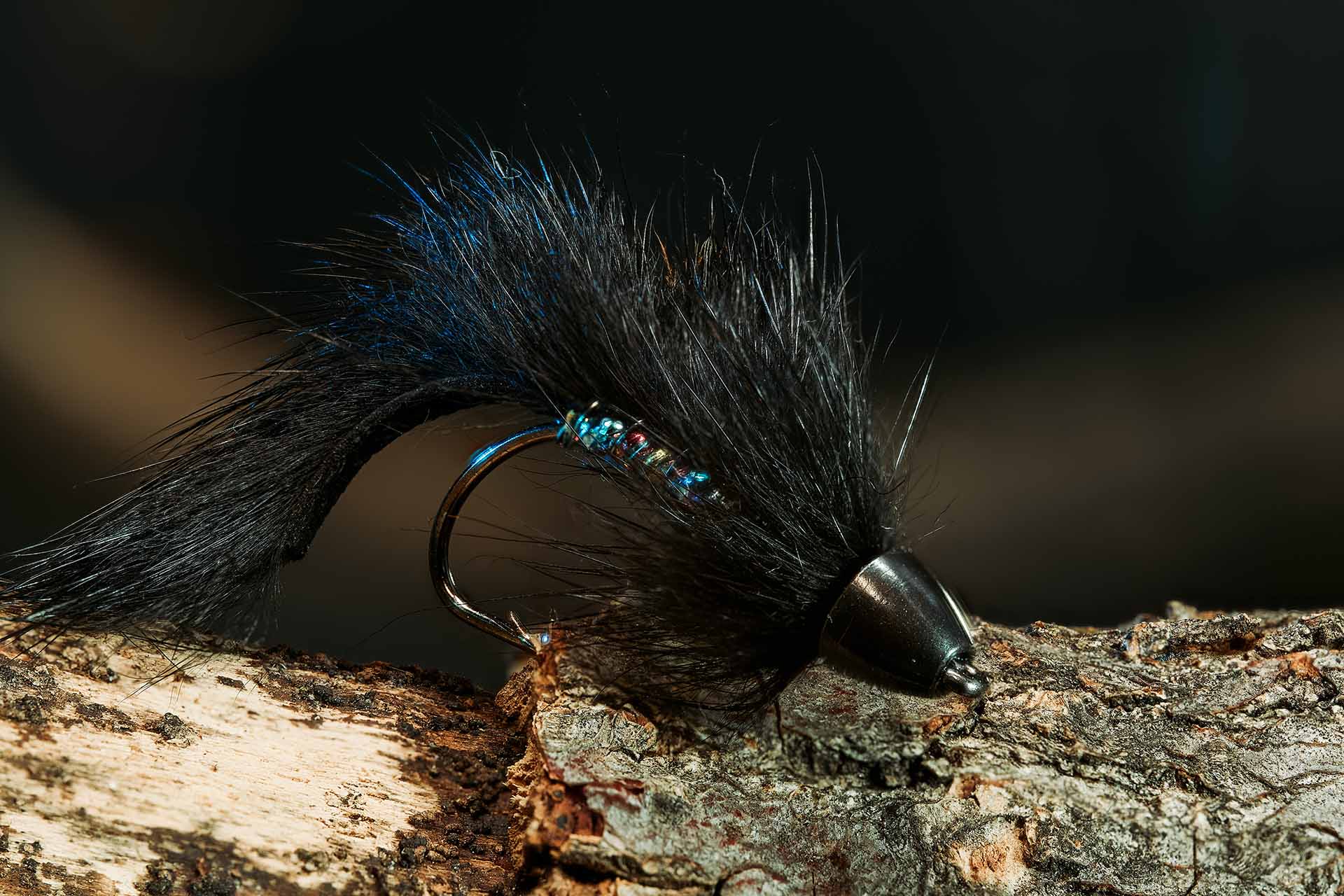Macro photo of a blue and black hand-tied fishing fly on a wood perch